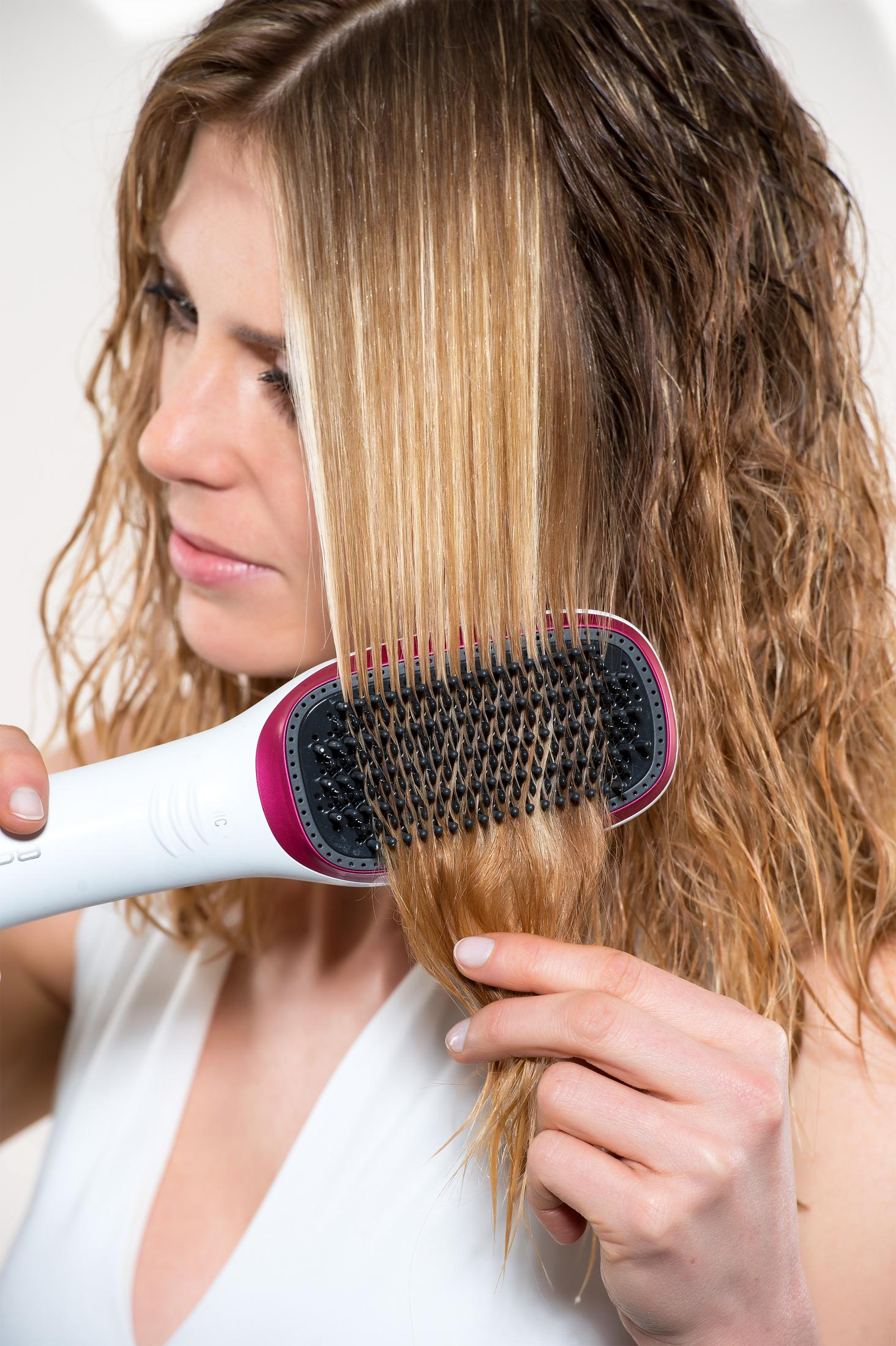 Una mujer se peina el pelo rubio y mojado con un peine blanco y rosa.