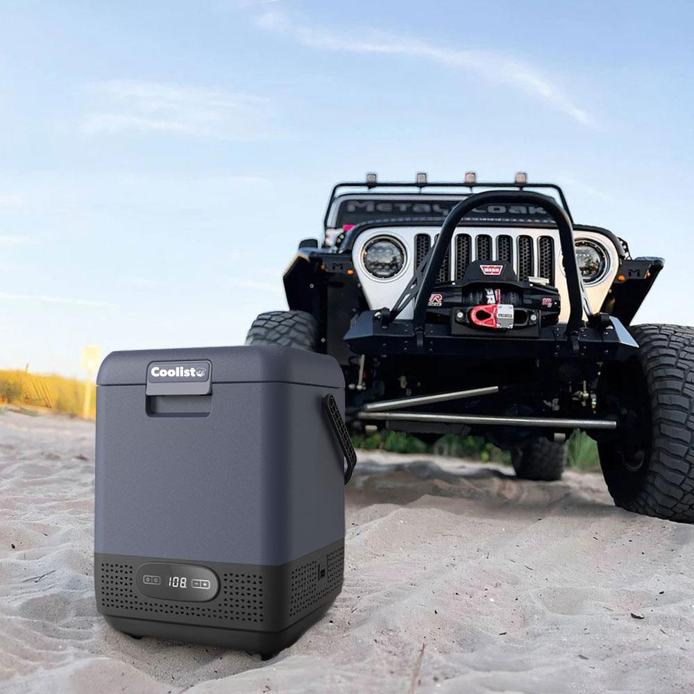 Mavi gökyüzü altında, modifiye edilmiş bir Jeep'in önünde kumda gri bir soğutucu.