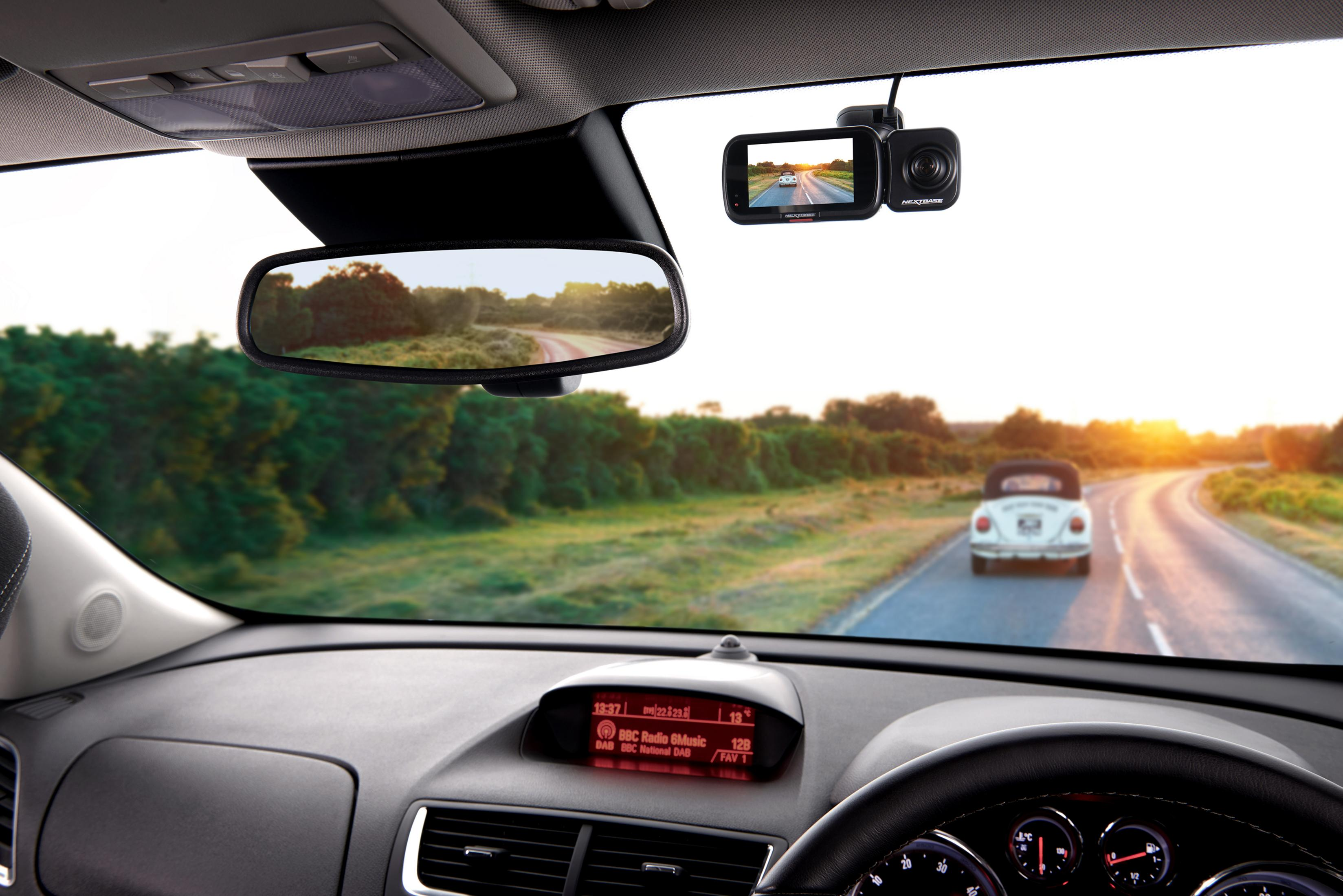 Innenansicht eines Autos mit Dashcam, das einem Oldtimer auf einer kurvigen Straße bei Sonnenuntergang folgt.