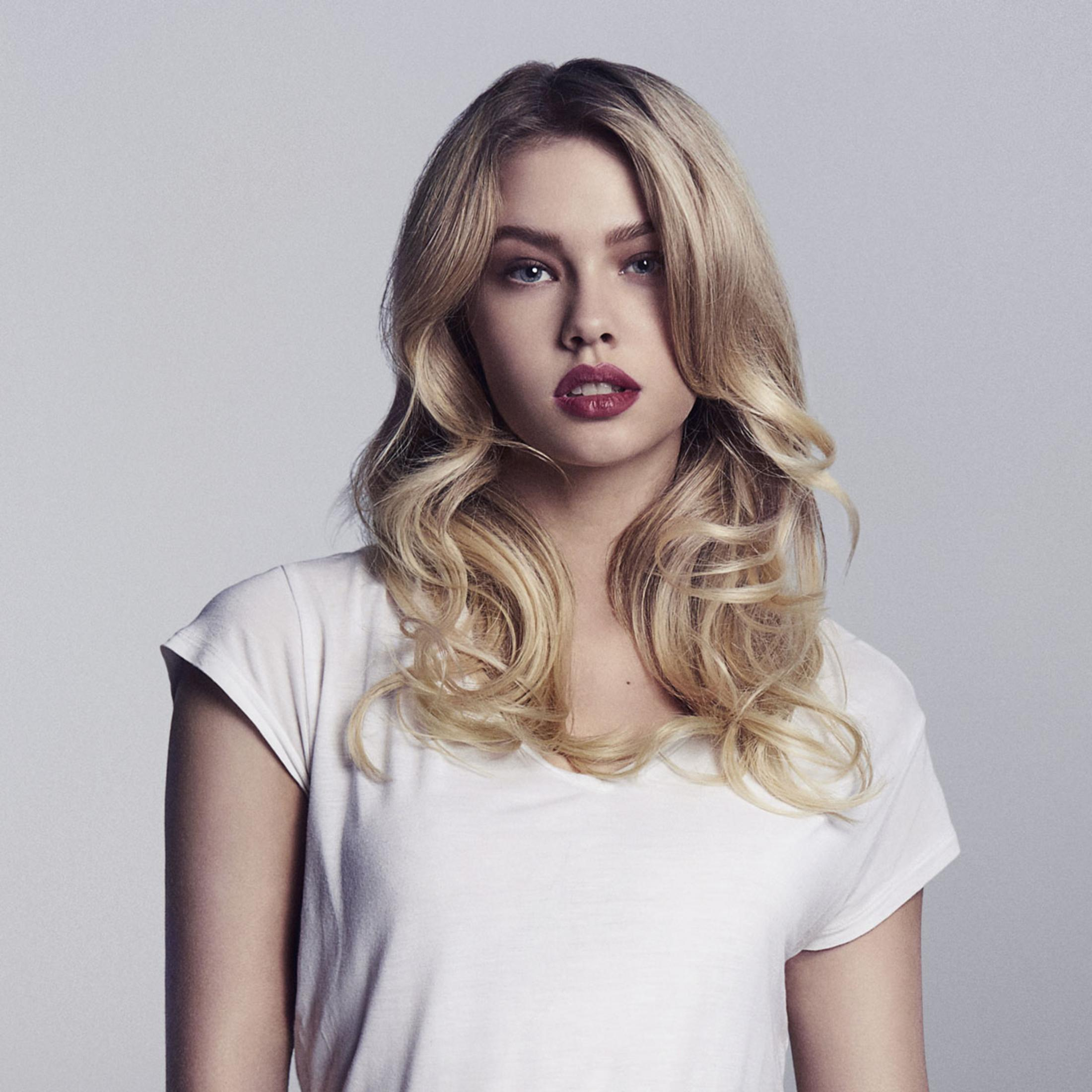 Eine Frau mit blonden Haaren und rotem Lippenstift trägt ein weißes T-Shirt.