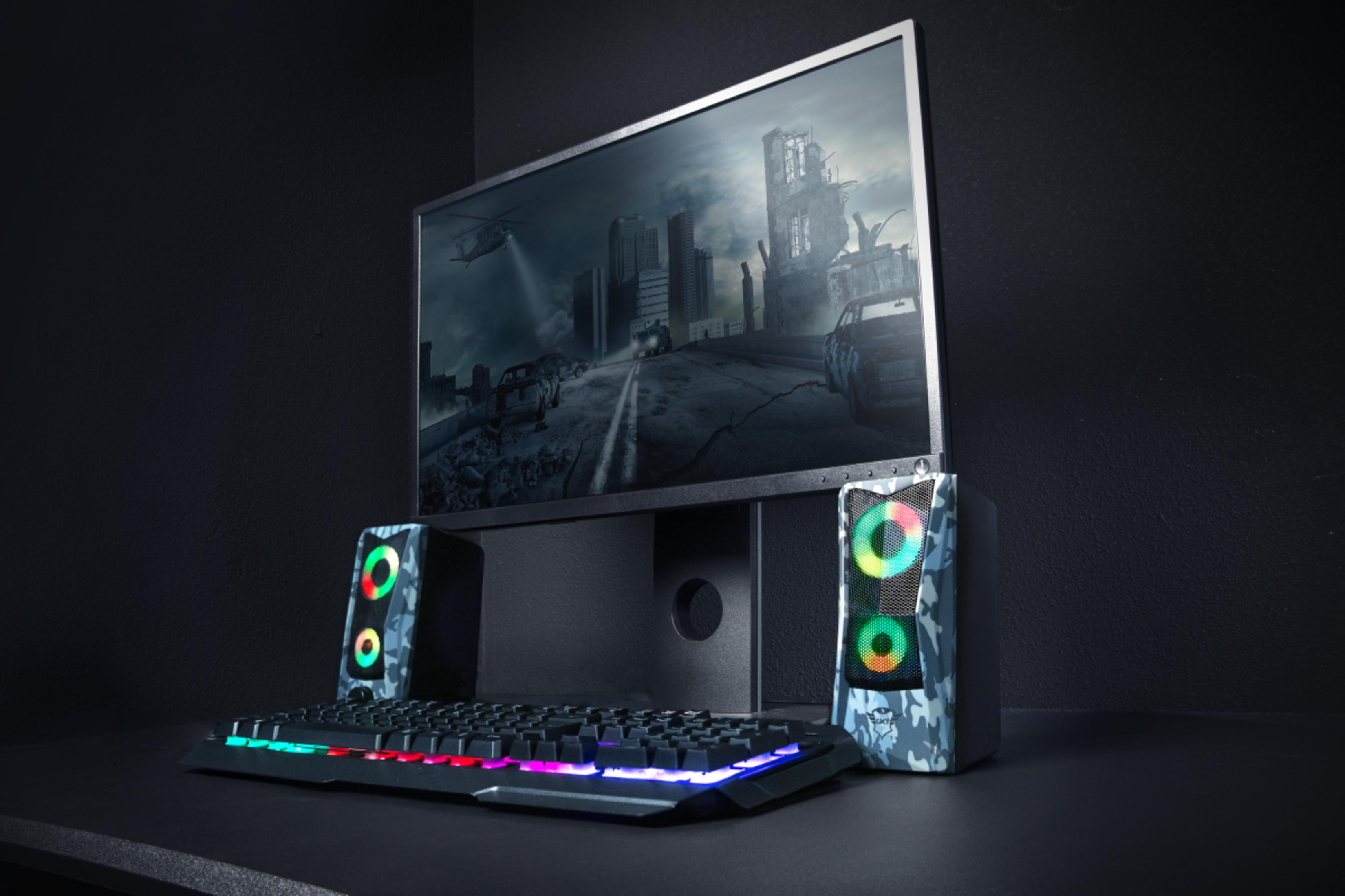 Un setup da gioco con tastiera illuminata, altoparlanti e un monitor che mostra una scena di città distopica.