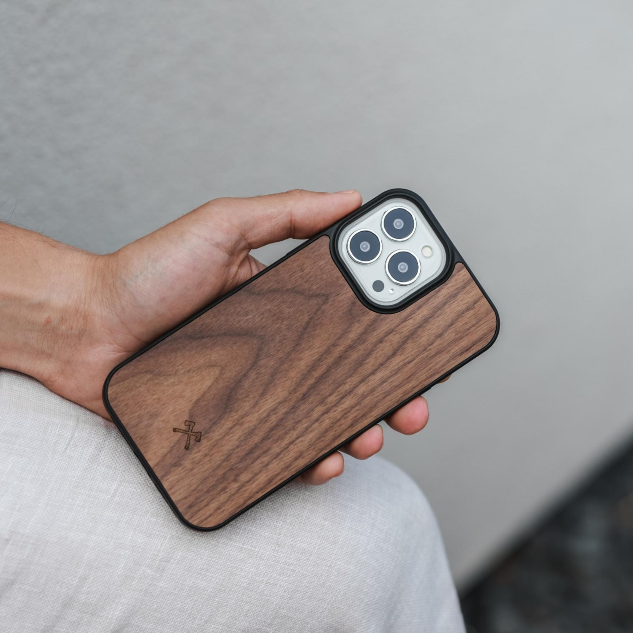 Eine Hand hält ein braunes Holz-iPhone-Gehäuse mit schwarzem Rand und Kameramodul.
