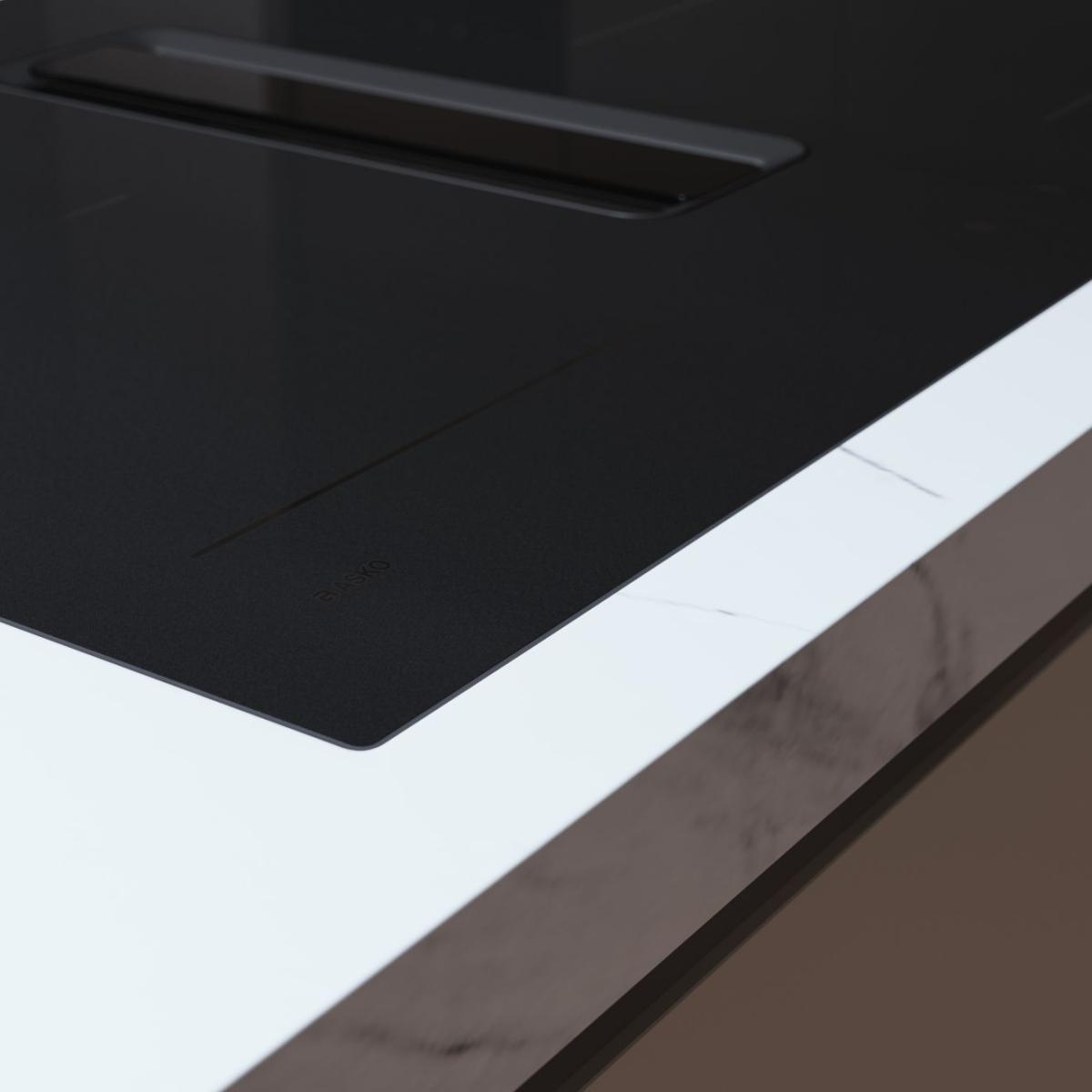 Un piano cottura a induzione nero con griglia di ventilazione integrata accanto a un piano di lavoro in marmo.
