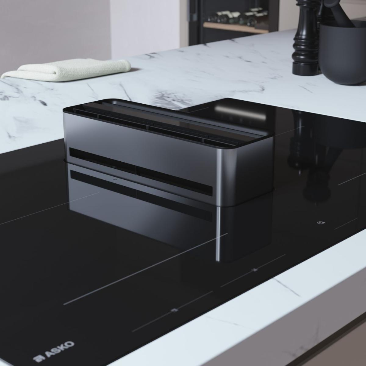 Un inserto cappa nero su un piano cottura a induzione nero con piano di lavoro in marmo.