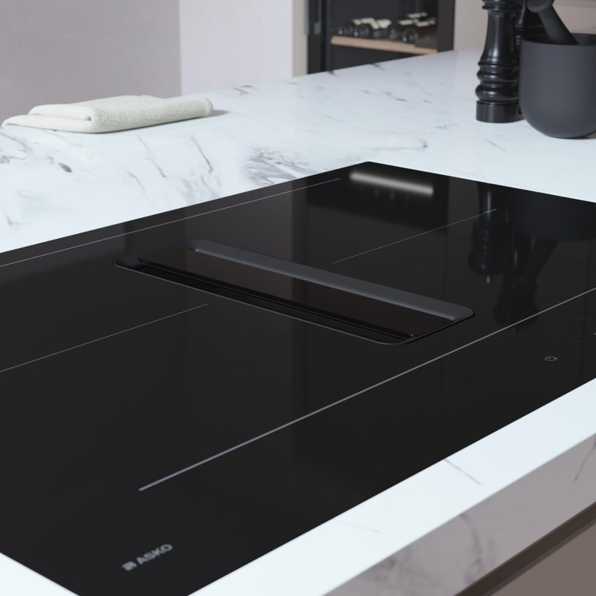 Un piano cottura a induzione nero moderno con cappa integrata su un piano di lavoro in marmo.
