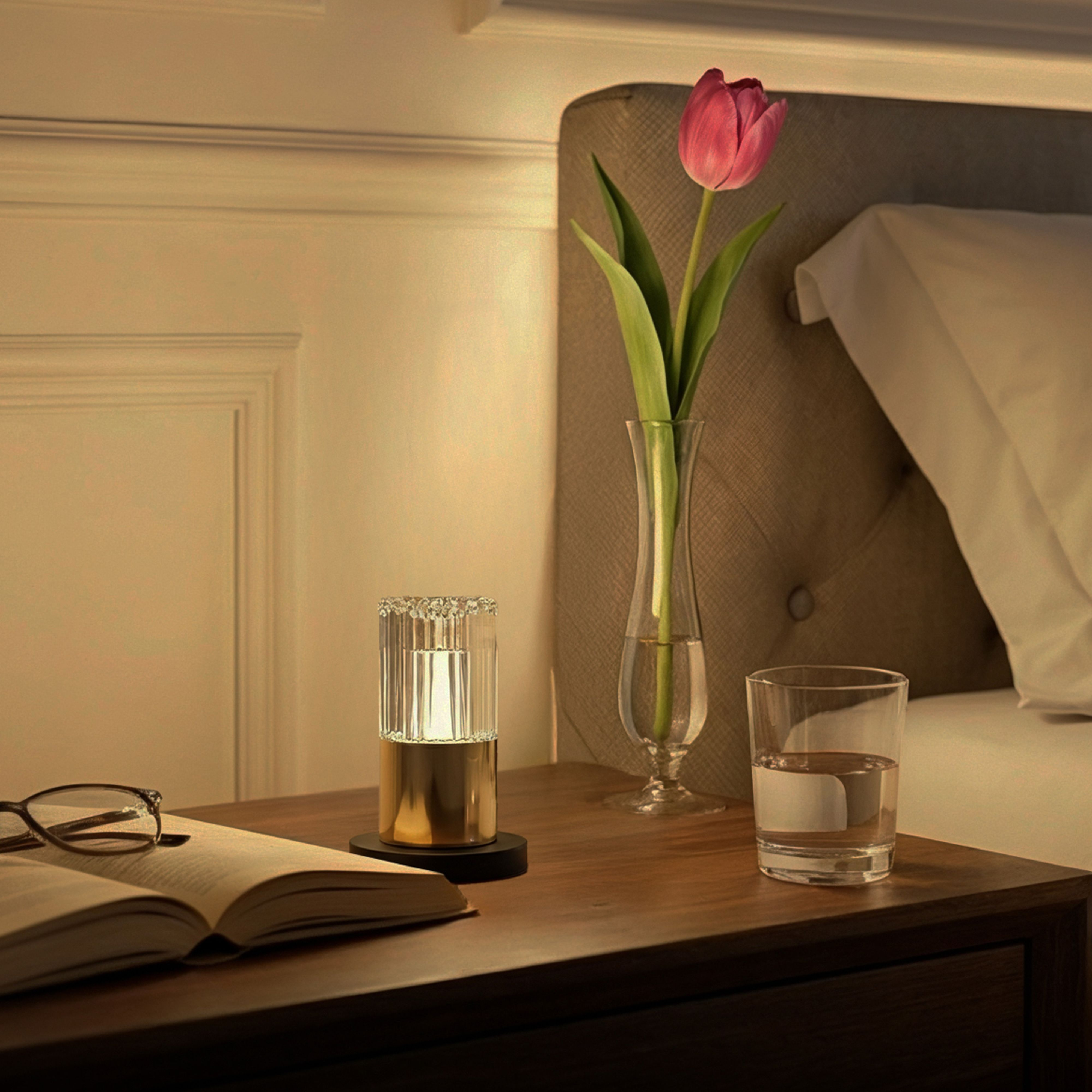 Ein Nachttisch mit Lampe, Glas Wasser, Brille und Buch.