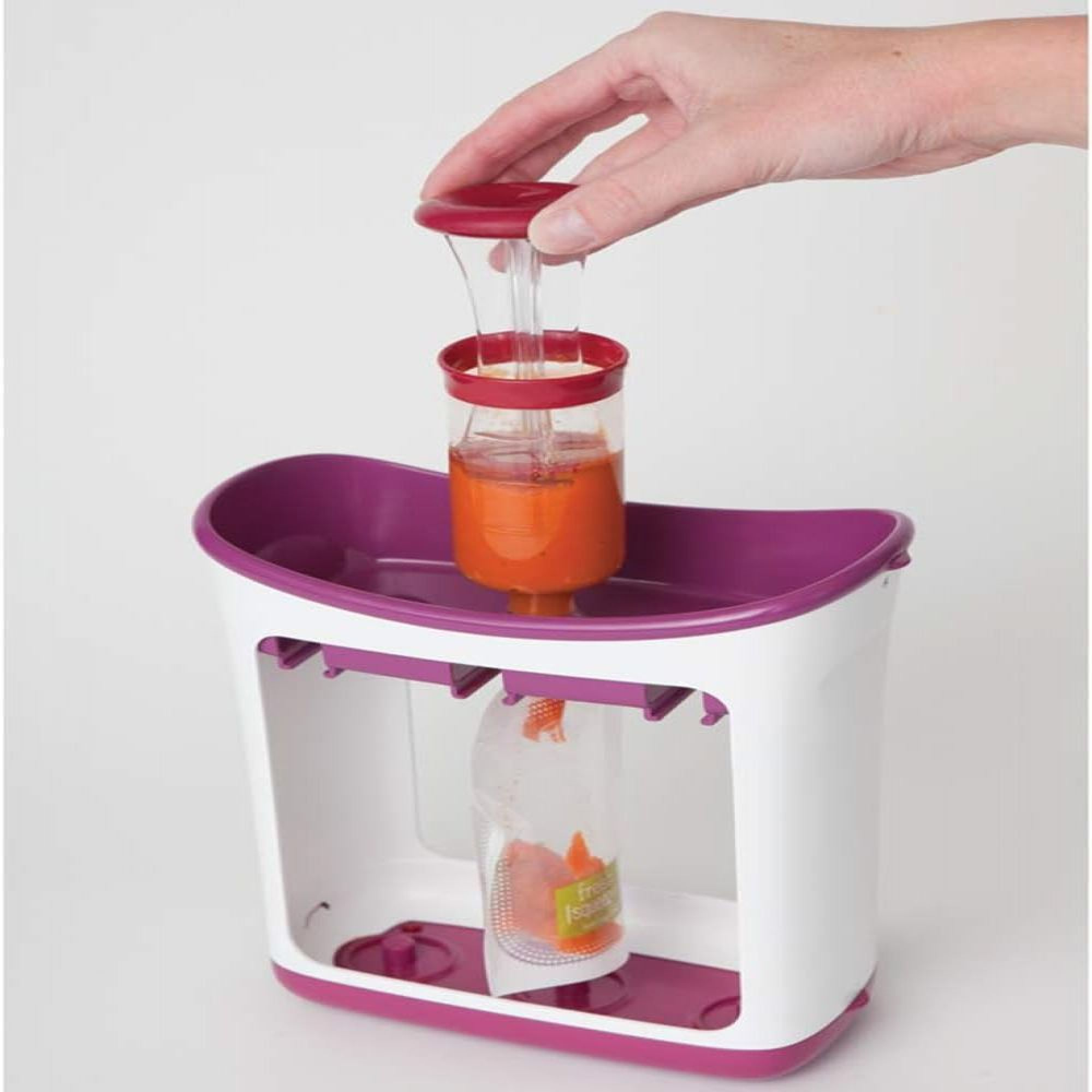 Ein Löffel füllt einen Beutel mit orangefarbener Babynahrung, der in einem weißen und lila Gerät steht.