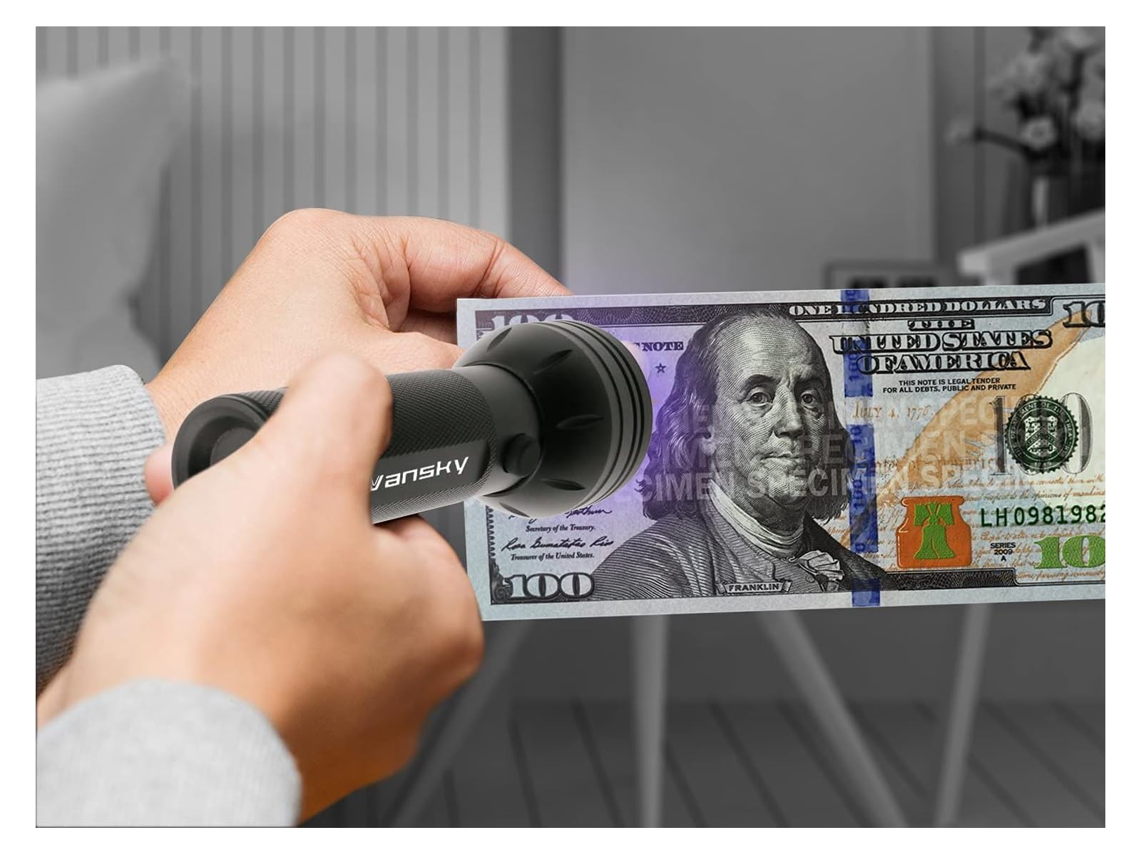 Eine Hand hält eine 100-Dollar-Note unter einer UV-Lampe.