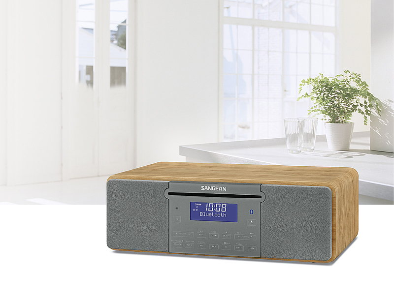 Une radio en placage bois avec haut-parleurs gris repose sur un comptoir blanc.