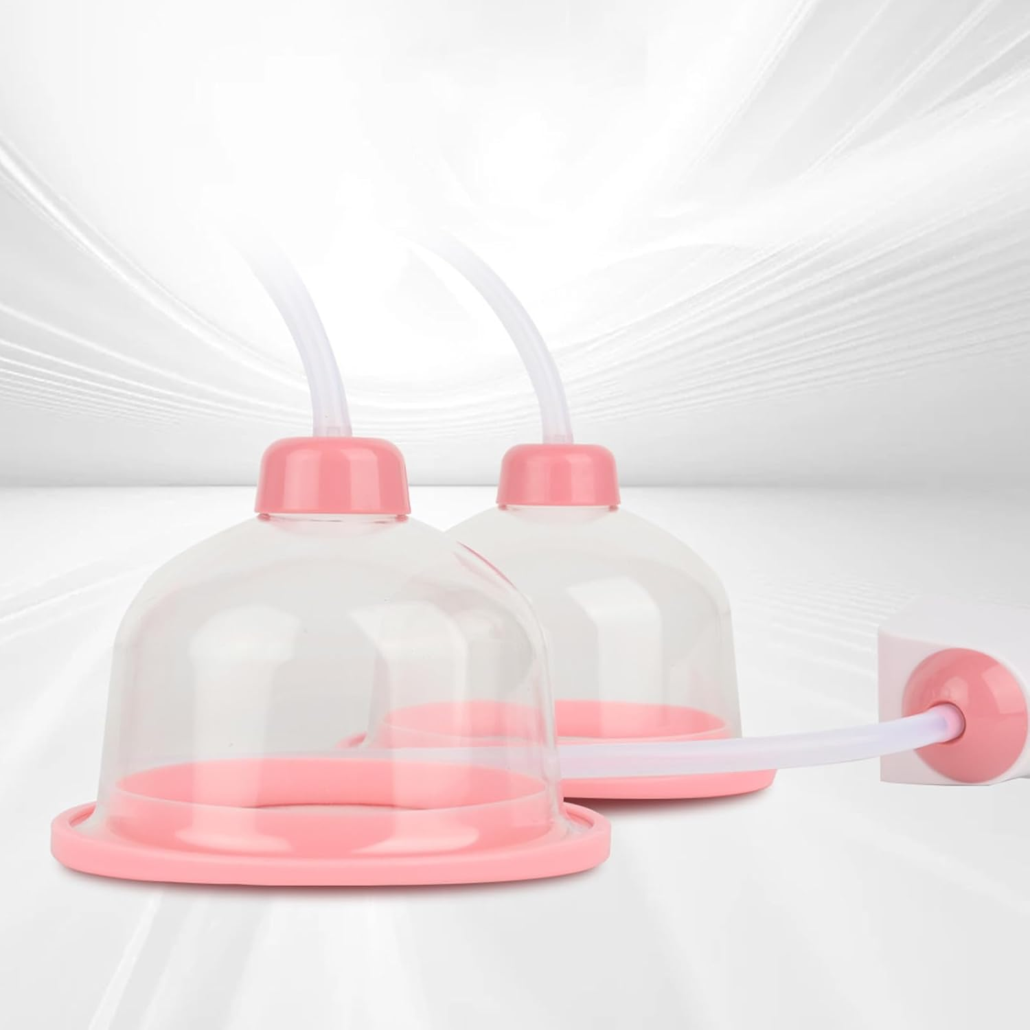 Zwei durchsichtige, rosa und weiße Saugglocken mit Schläuchen auf weißem Hintergrund.