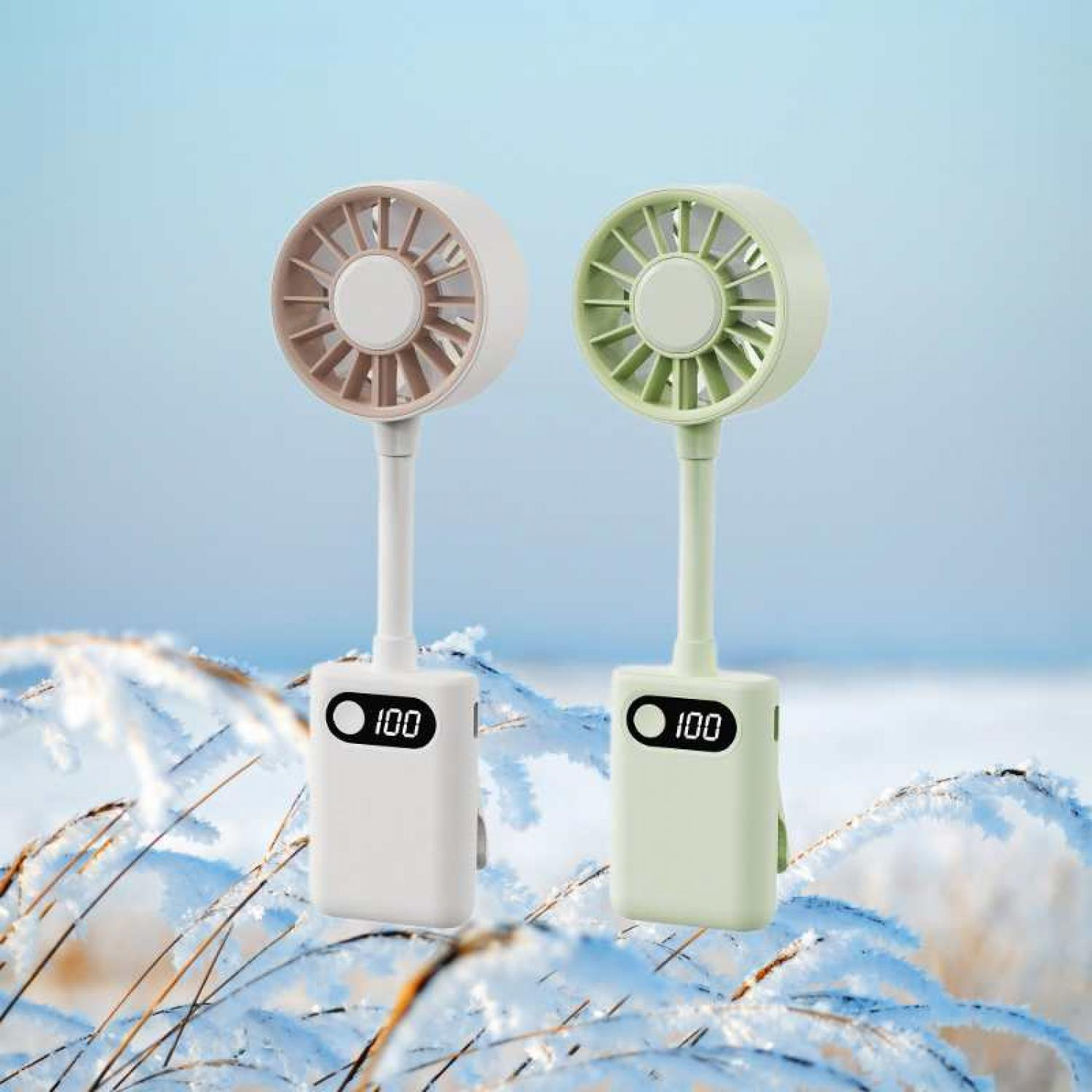 Zwei tragbare Ventilatoren, einer beige und einer hellgrün, mit Digitalanzeigen, stehen auf verschneiten Ästen.