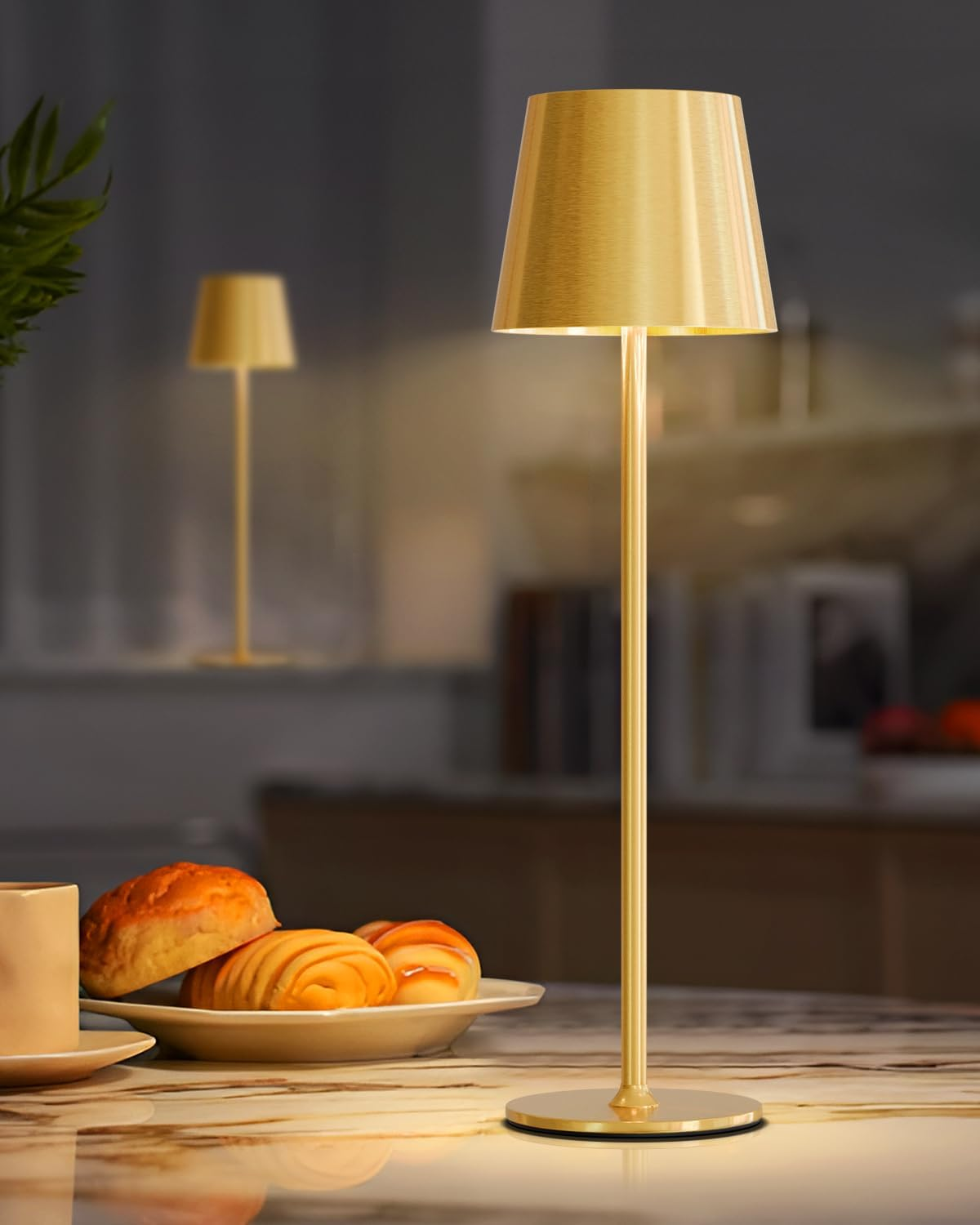 Goldene Lampe auf einem Marmortisch neben Gebäck. Ein weiterer Lampenspiegel im Hintergrund.