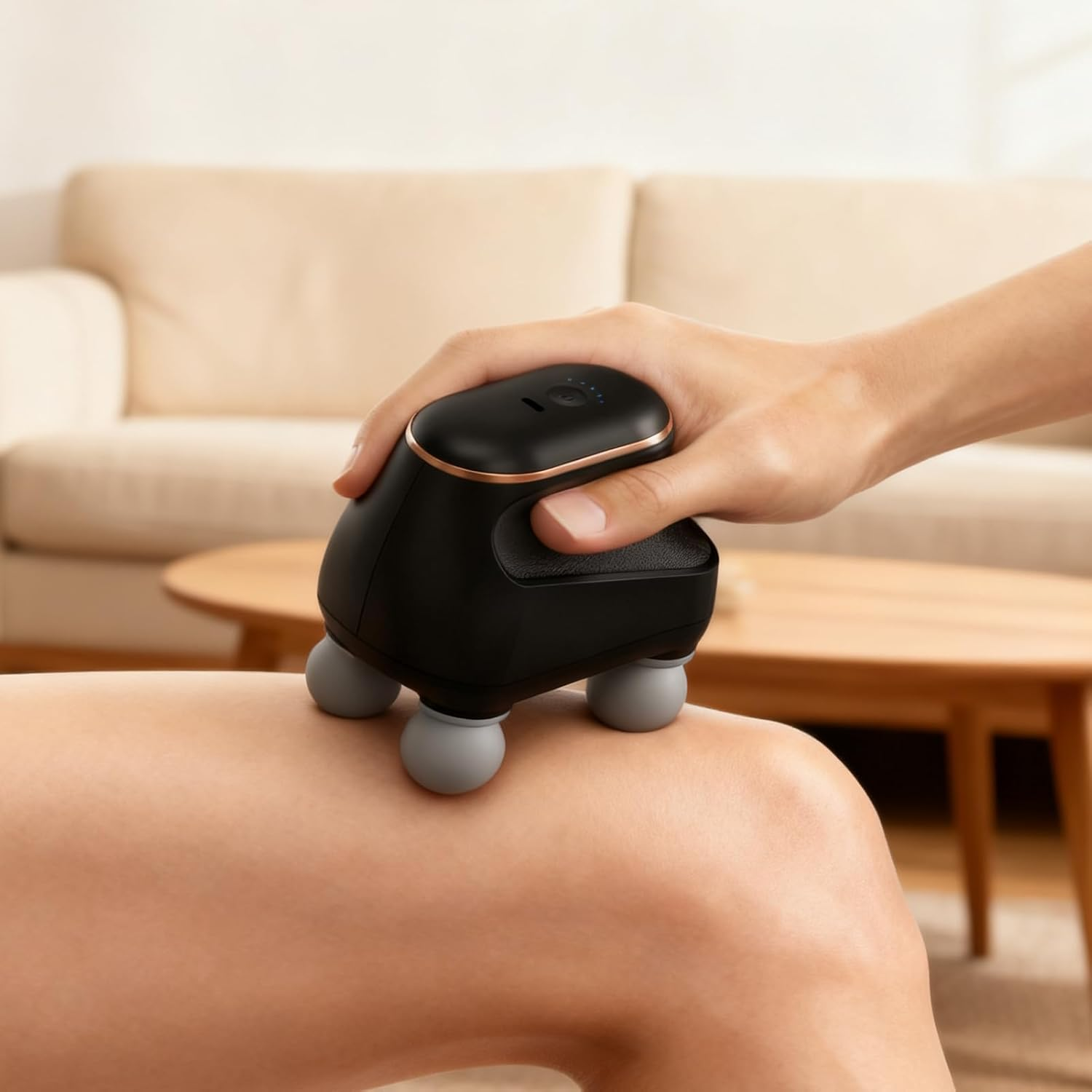 Hand hält Massagegerät mit Kugeln auf Bein. Couch im Hintergrund.