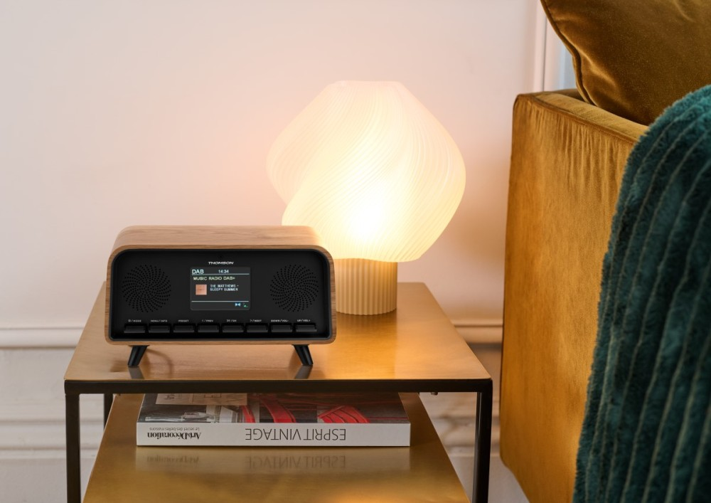 Una radio DAB in legno si trova su un comodino accanto a una lampada e un divano.