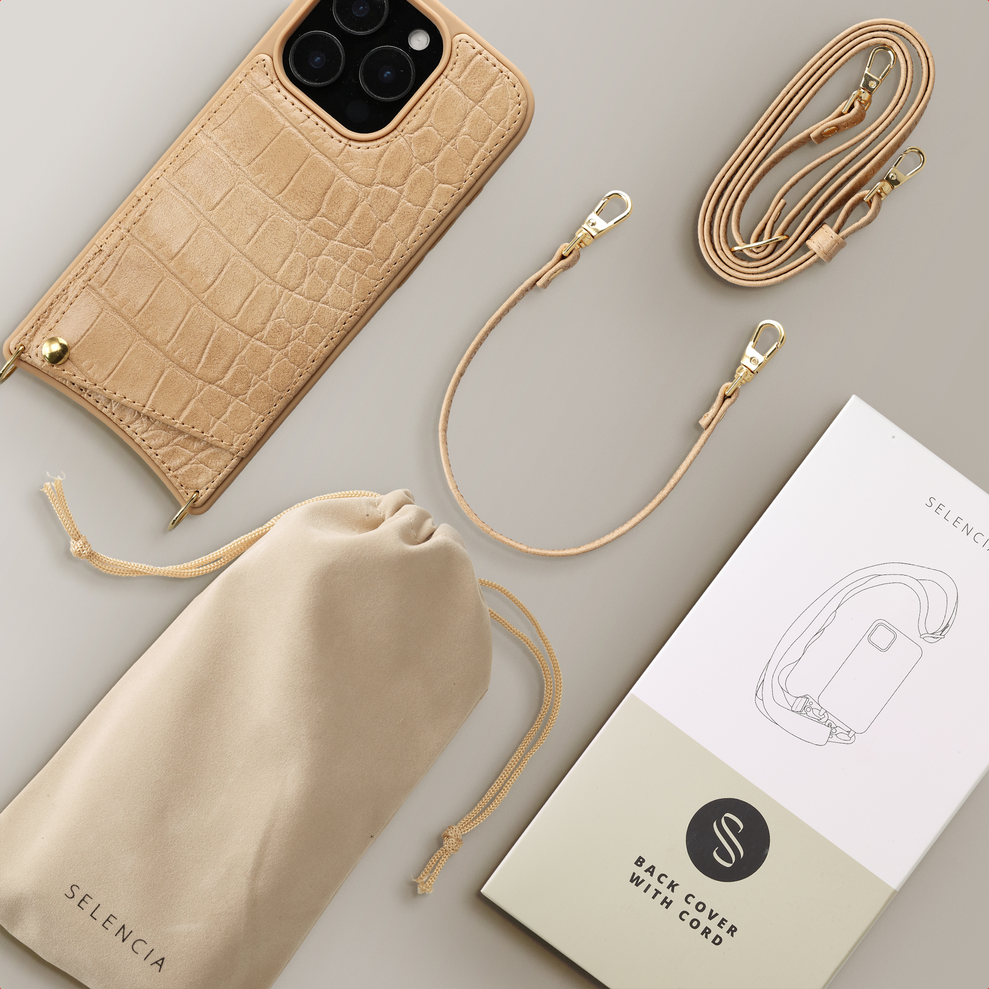 Une coque de téléphone en cuir de crocodile beige avec une lanière, une pochette et une boîte.