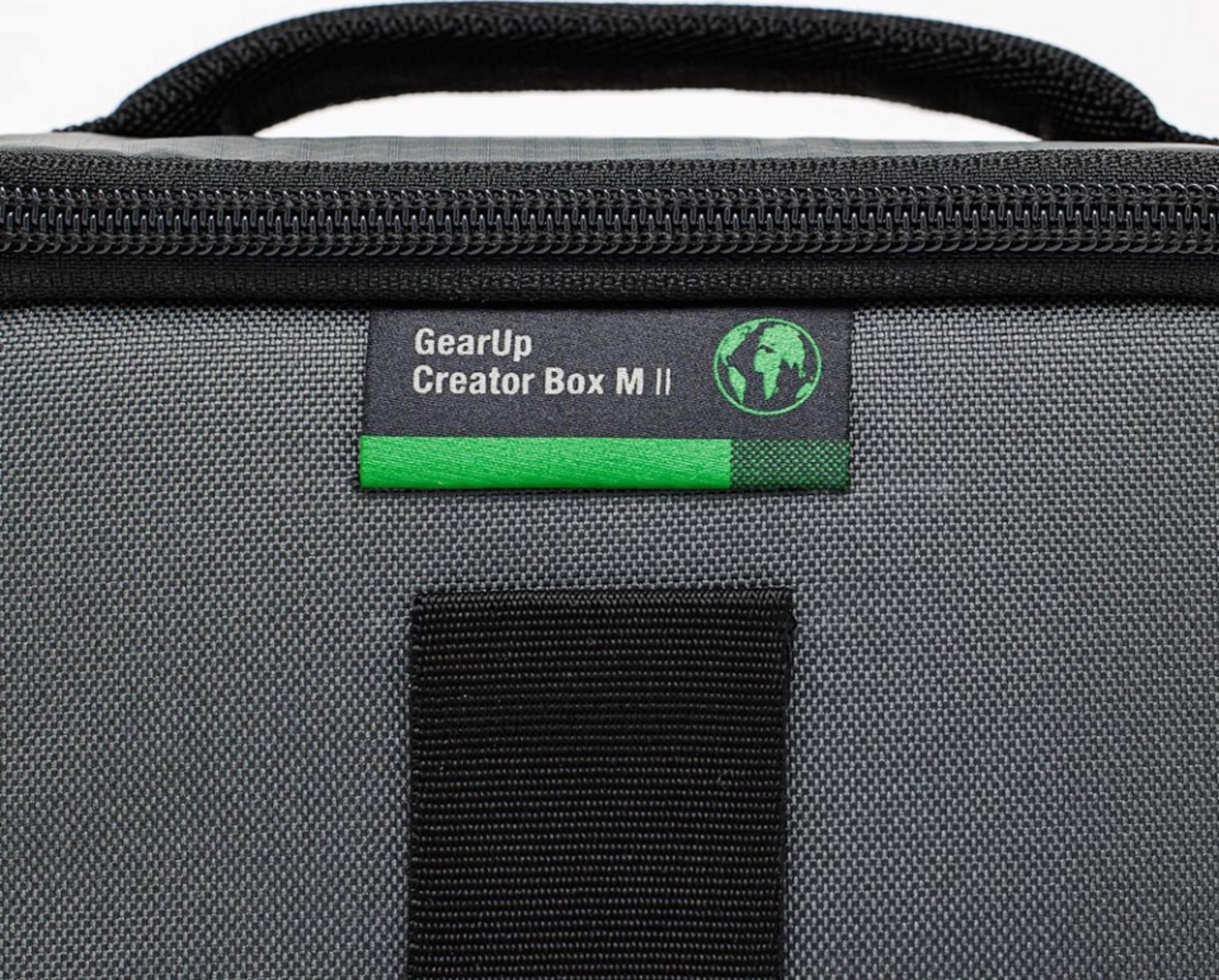 Graue Tasche mit schwarzem Reißverschluss und einem grünen Label mit Erdlogo.