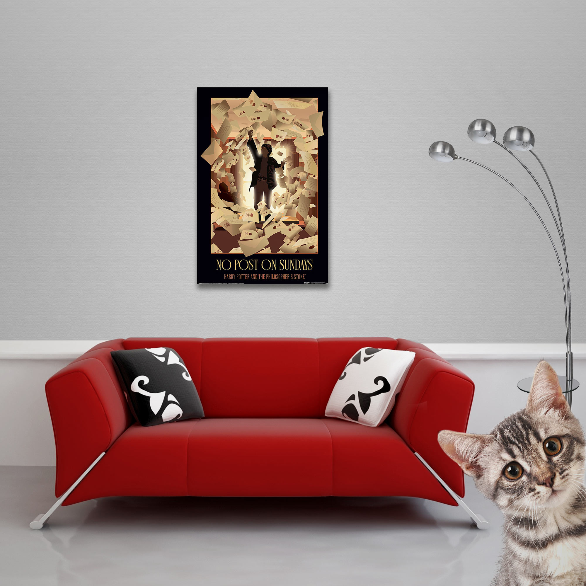 Ein Kater schaut über ein rotes Sofa. Ein Poster hängt an der Wand.