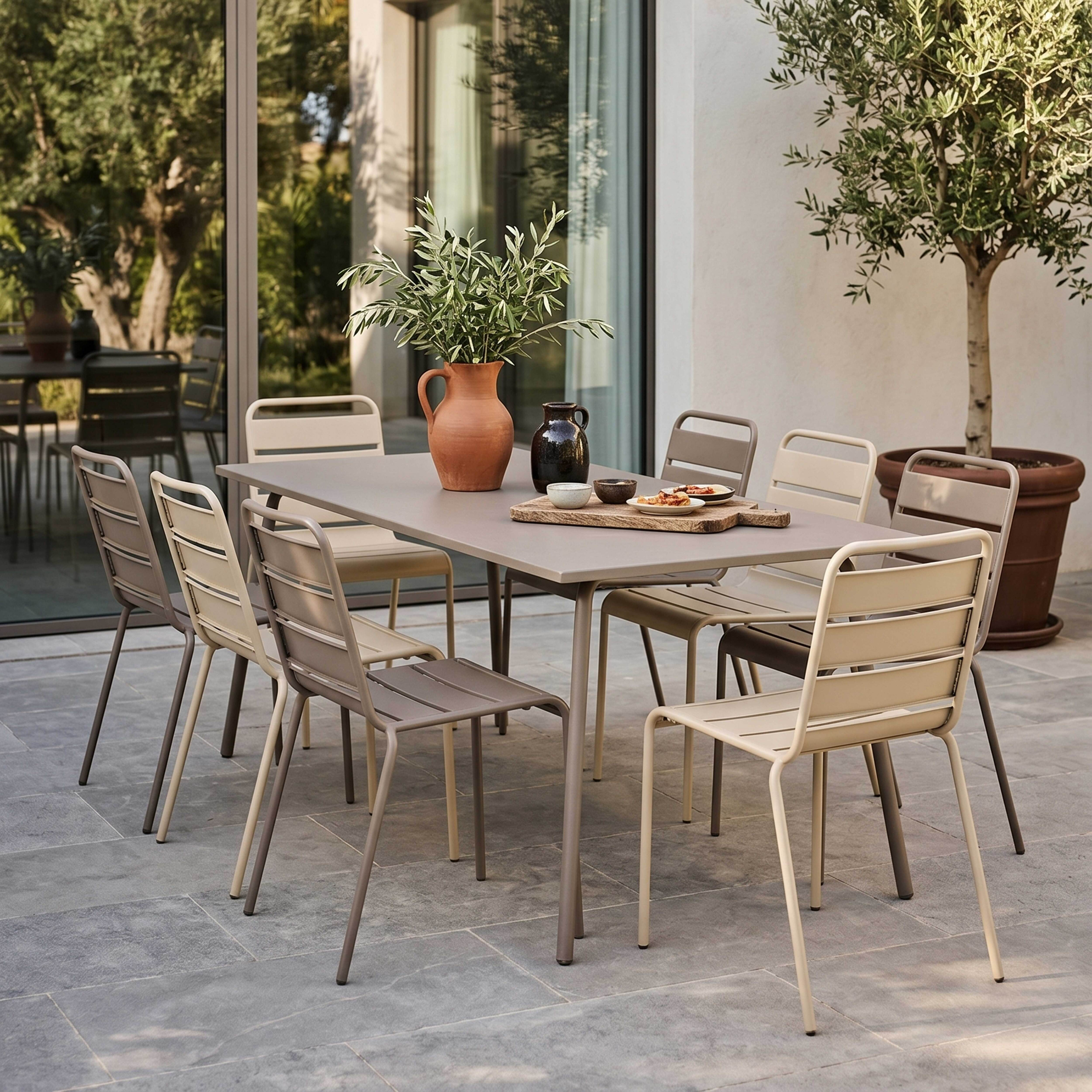Gedeckter Tisch mit Stühlen im Freien, mit Terrakotta-Vase, Keramik und Speisen.