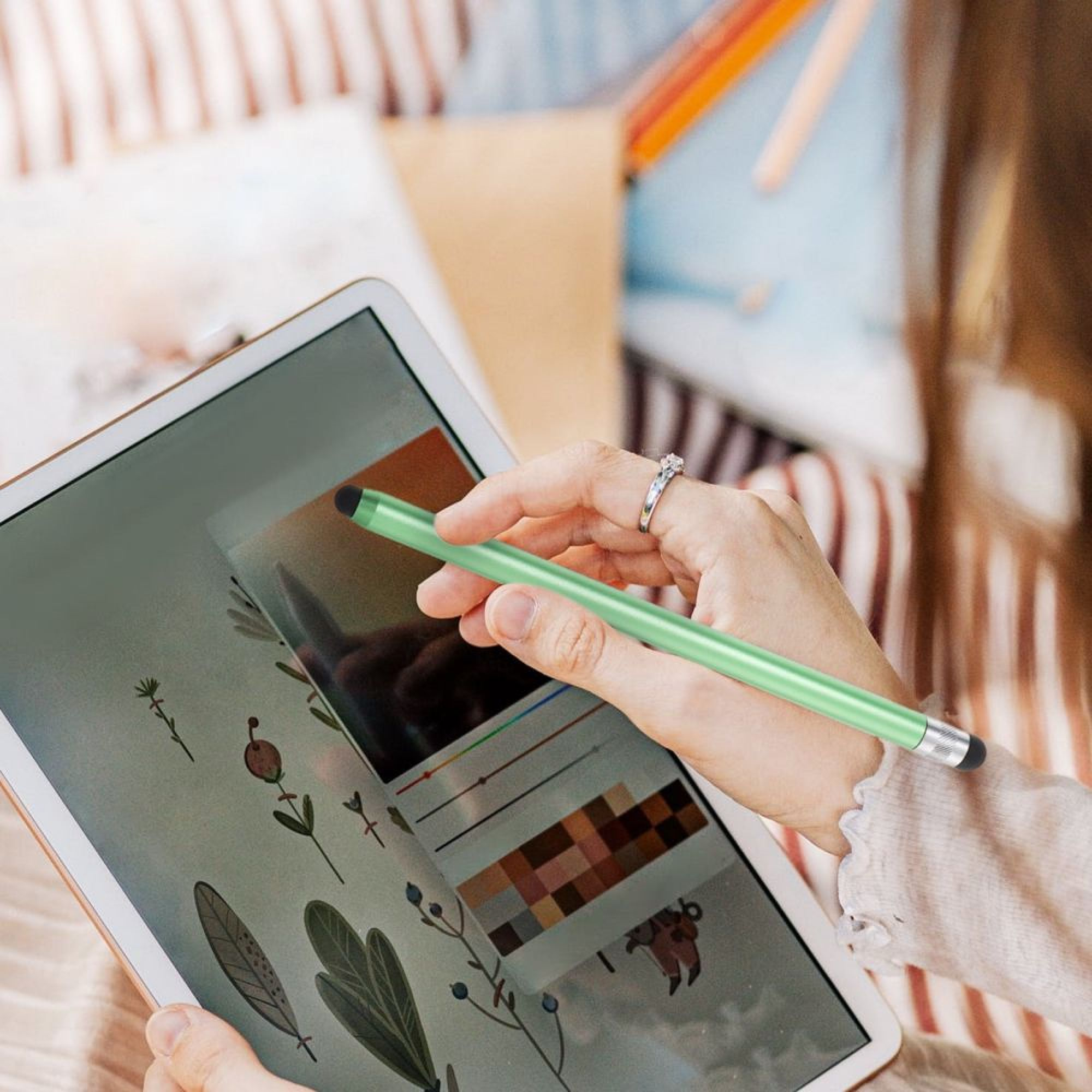 Eine Hand benutzt einen grünen Stift auf einem Tablet mit botanischen Illustrationen.