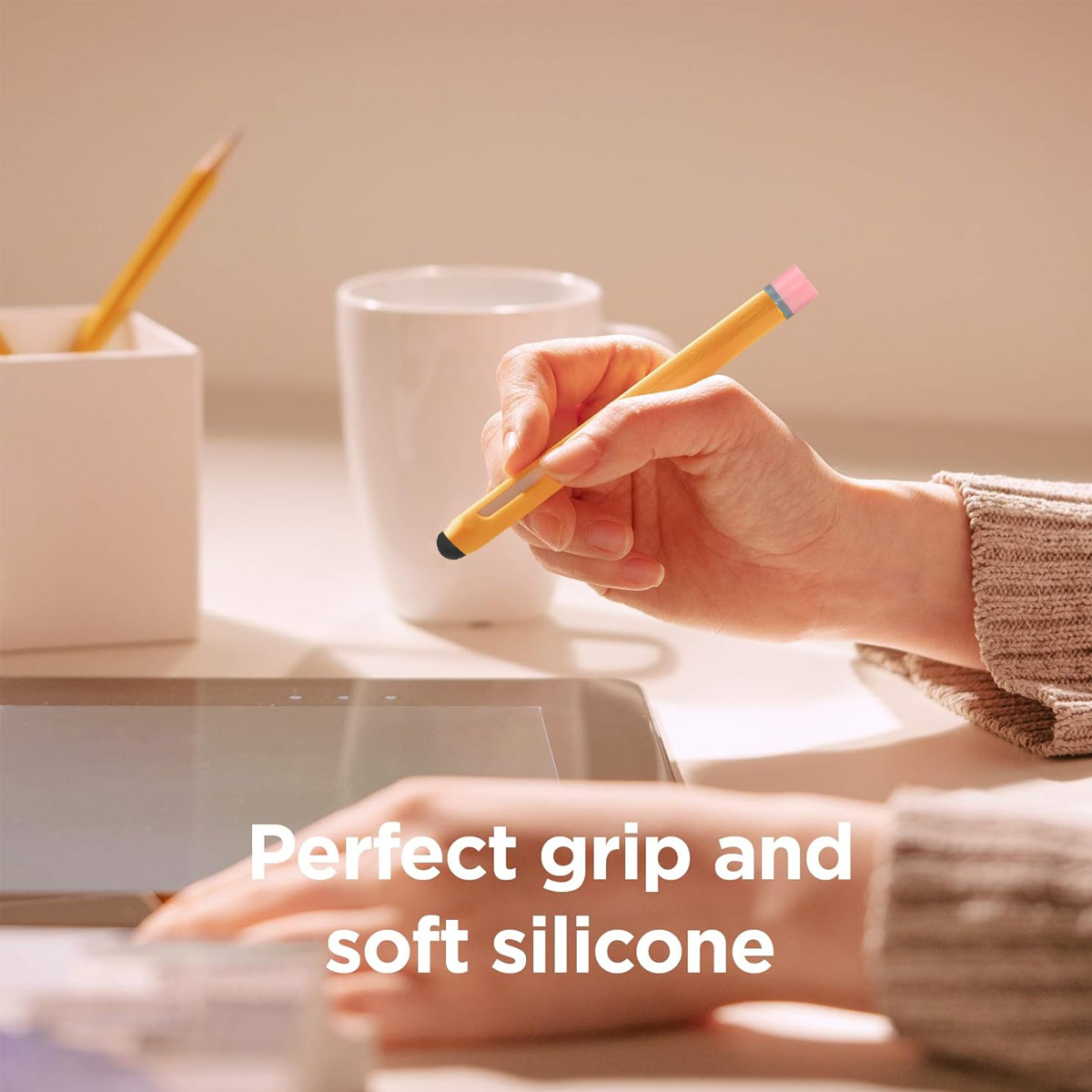 Eine Hand hält einen gelben Stift über einem Tablet. Tasse und Bleistifte im Hintergrund.