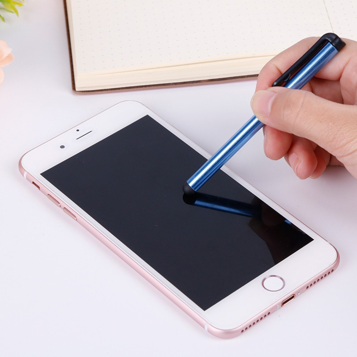 Eine Hand hält einen blauen Stift über den Bildschirm eines roségoldenen Smartphones.