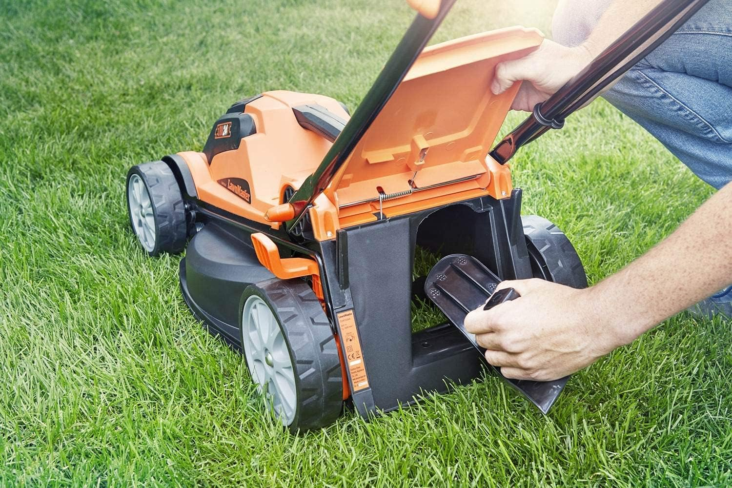 Mann mit Jeans setzt orange Mähkorb in Rasenmäher auf grünem Gras ein.