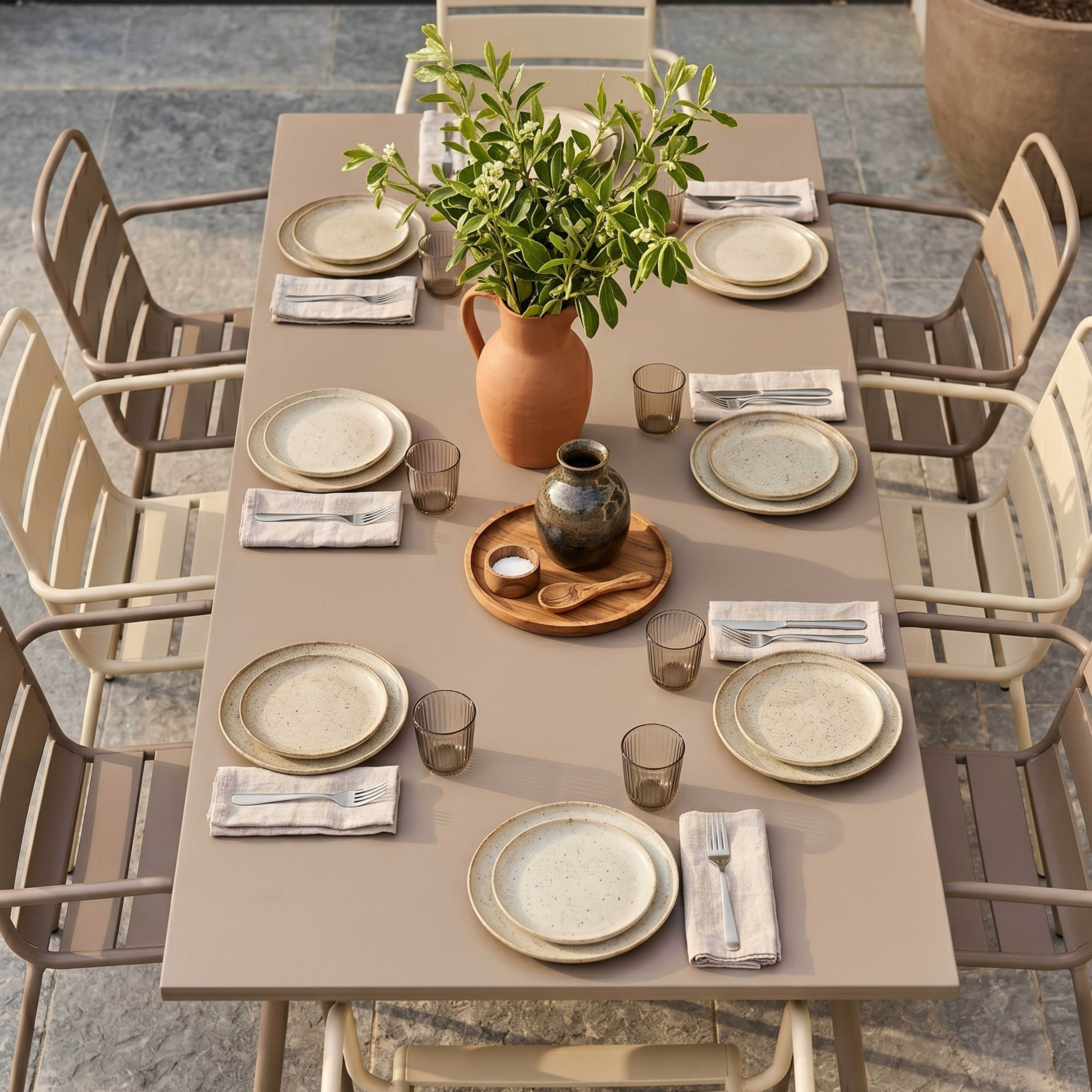 Gedeckter Tisch im Freien mit Tellern, Gläsern, Besteck und einem Blumenstrauß.