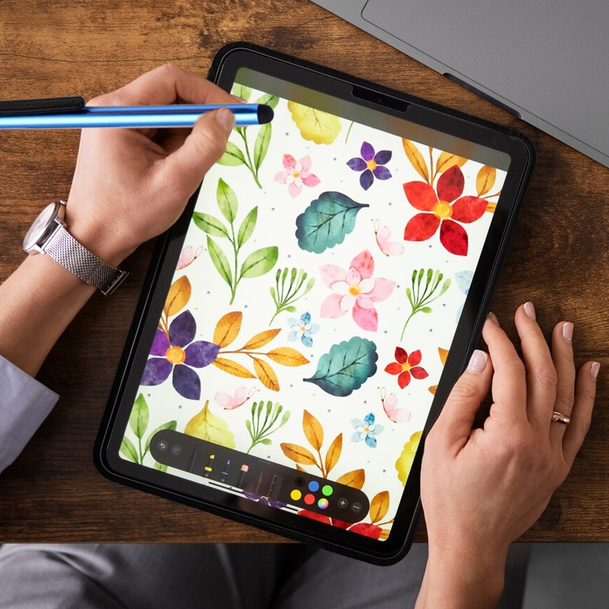 Eine Person nutzt einen blauen Stift, um auf einem Tablet mit Blumenmuster zu zeichnen.