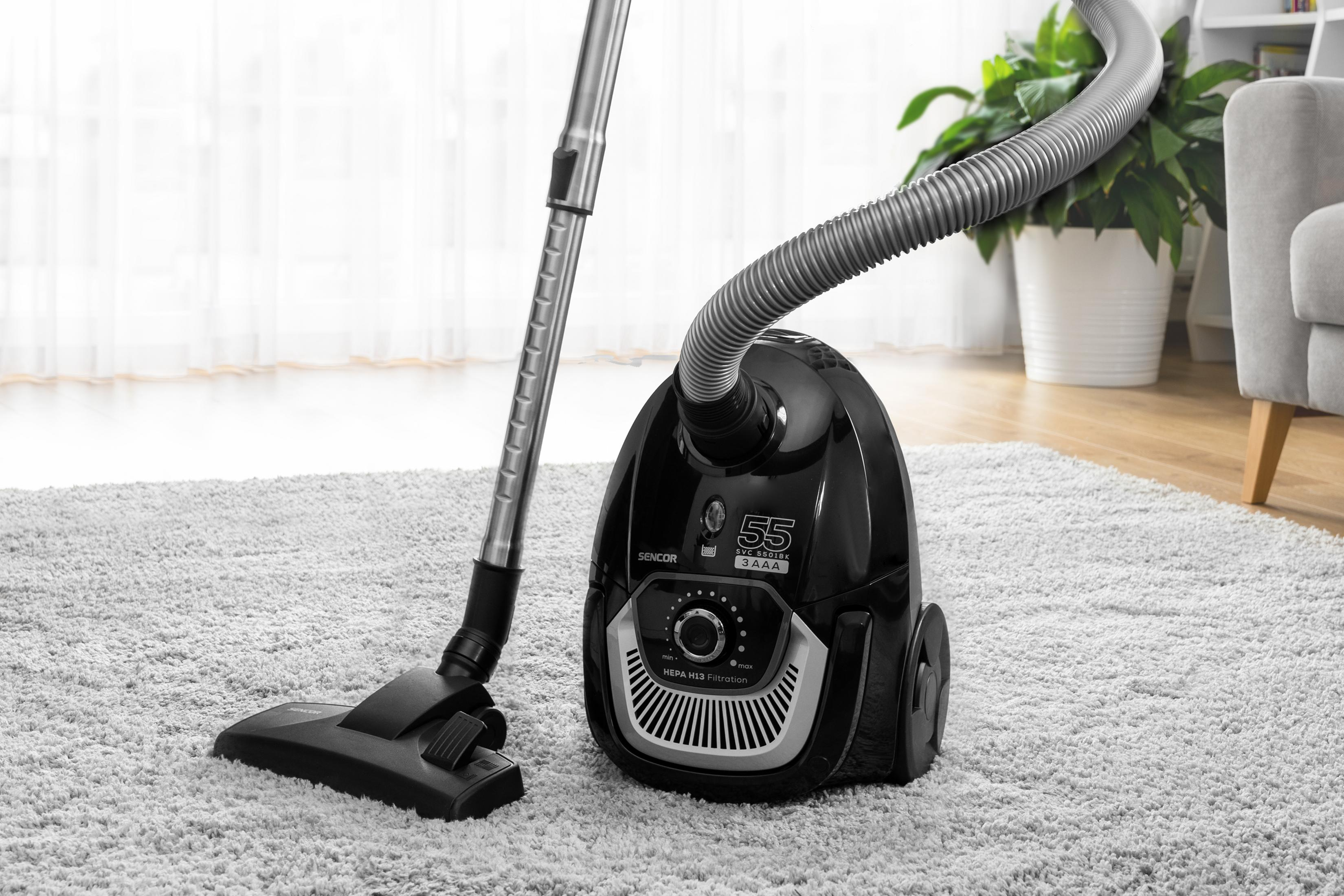 Schwarzer Staubsauger auf grauem Teppich mit silbernem Rohr und Schlauch.