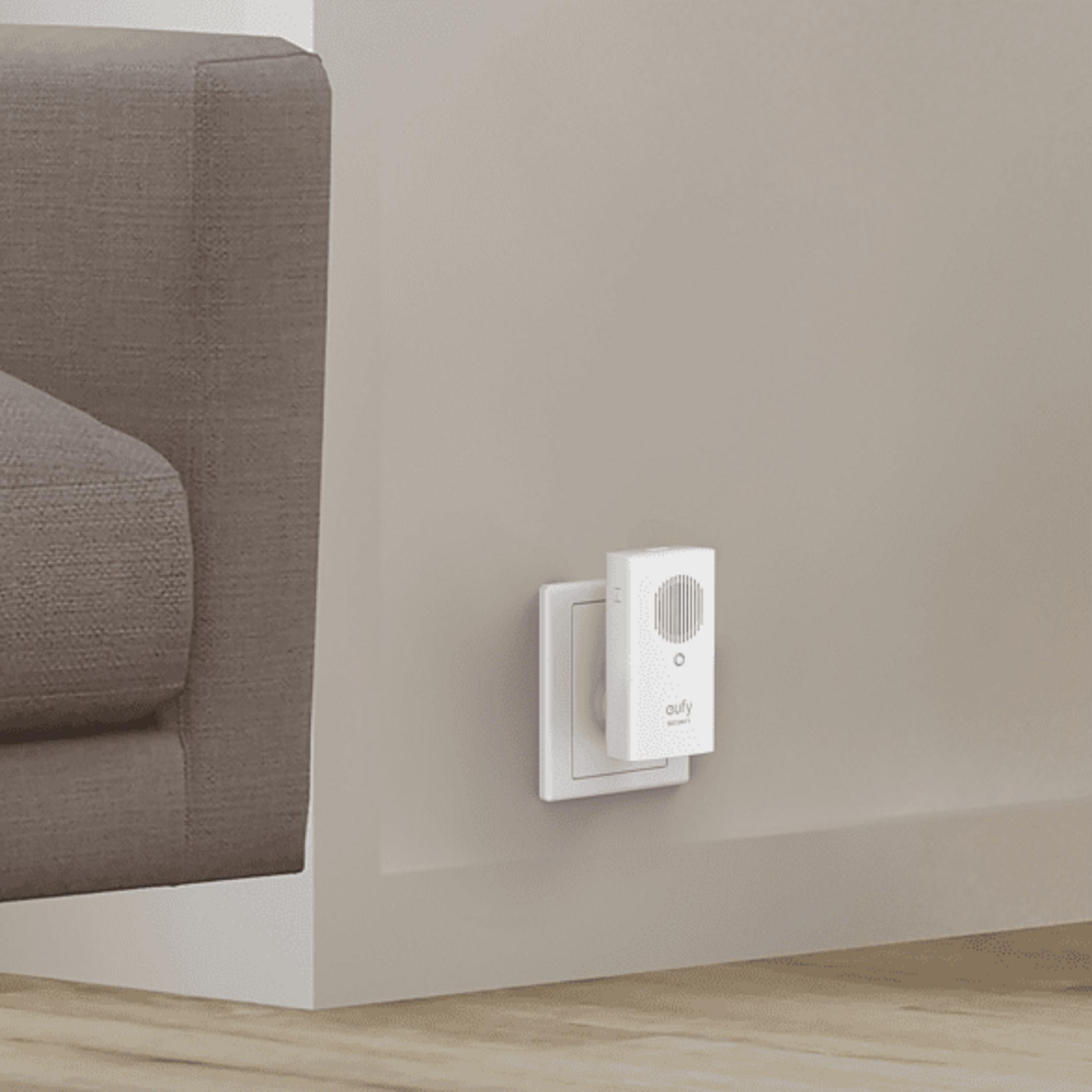 Ein weißer Stecker mit EU-Adapter steckt in einer Wandsteckdose neben einem Sofa.
