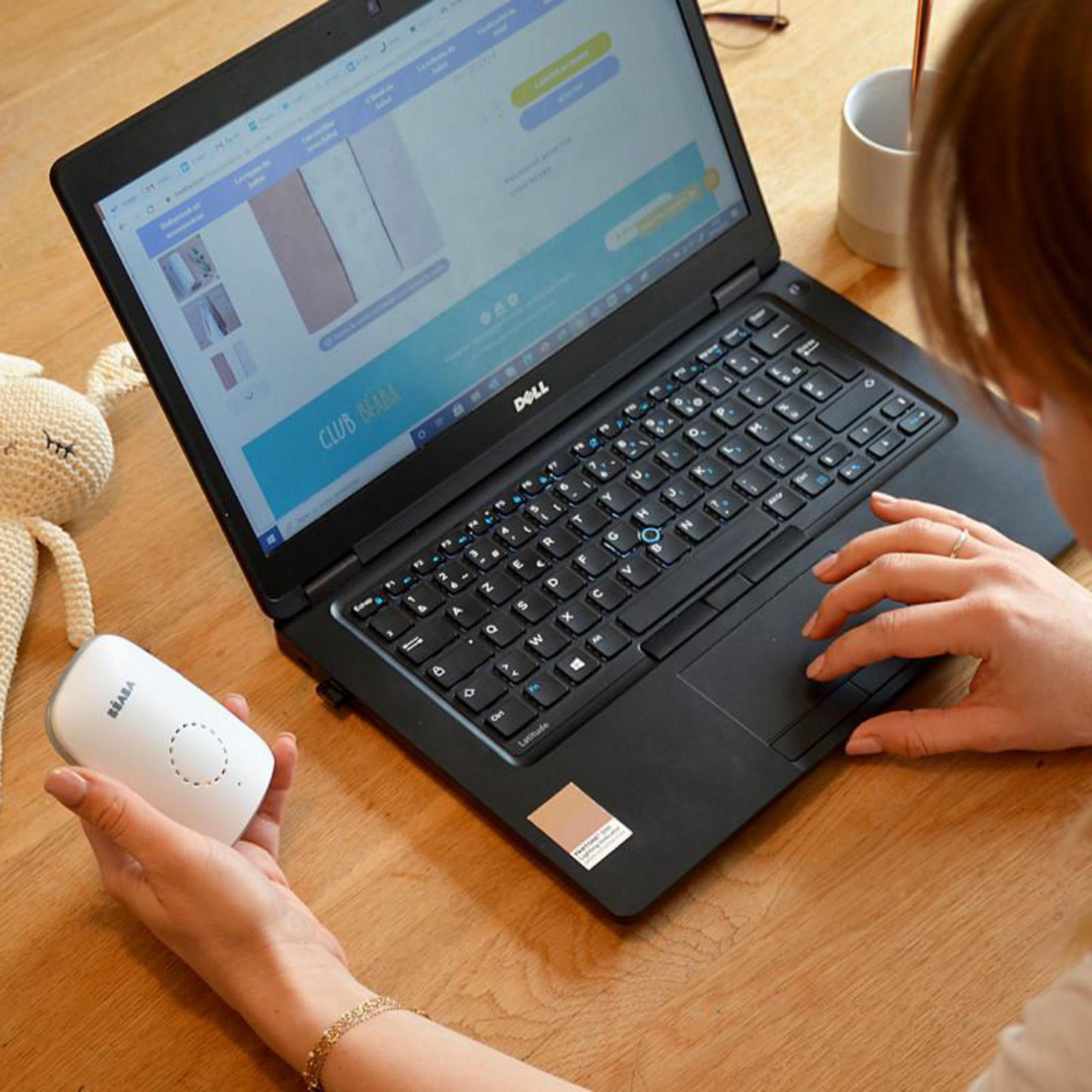 Eine Person benutzt einen Laptop und hält ein weißes Gerät. Ein Stoffhasenspielzeug ist sichtbar.
