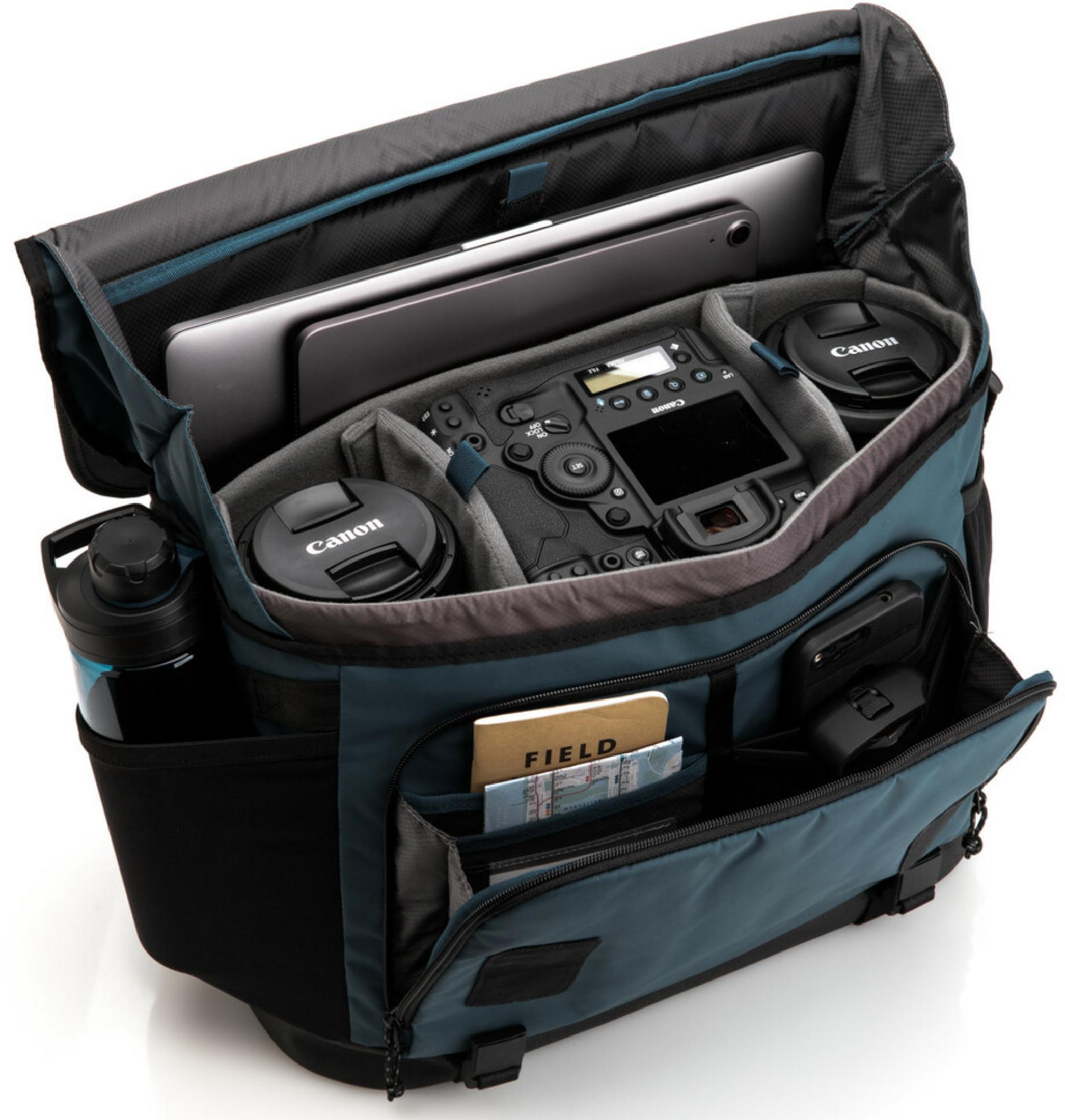 Een camerateas met laptop, camera, lensdoppen, waterfles en notitieboek erin.