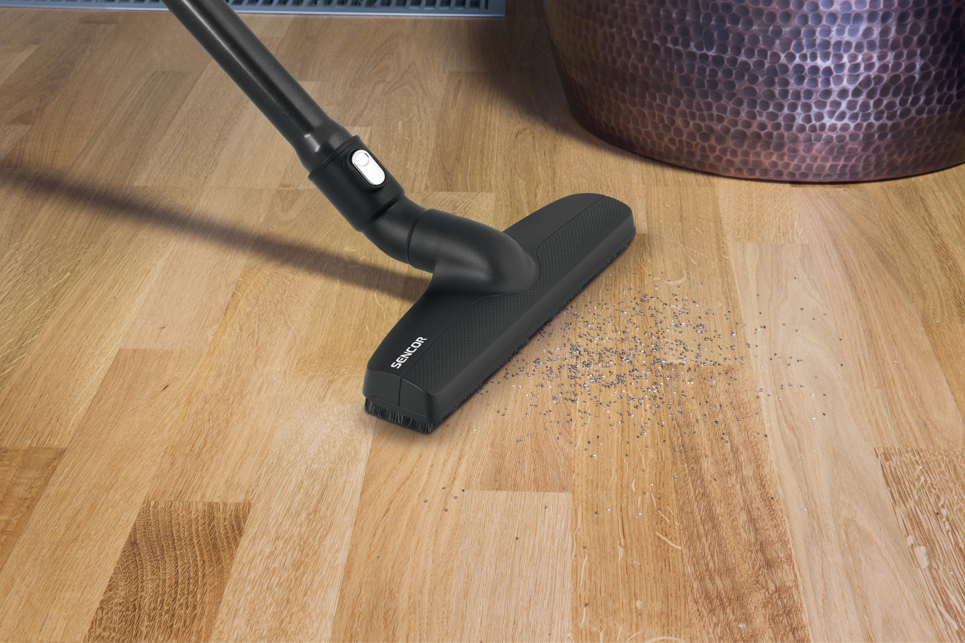 Un cabezal de aspiradora negro limpia pequeñas partículas de un suelo de madera.