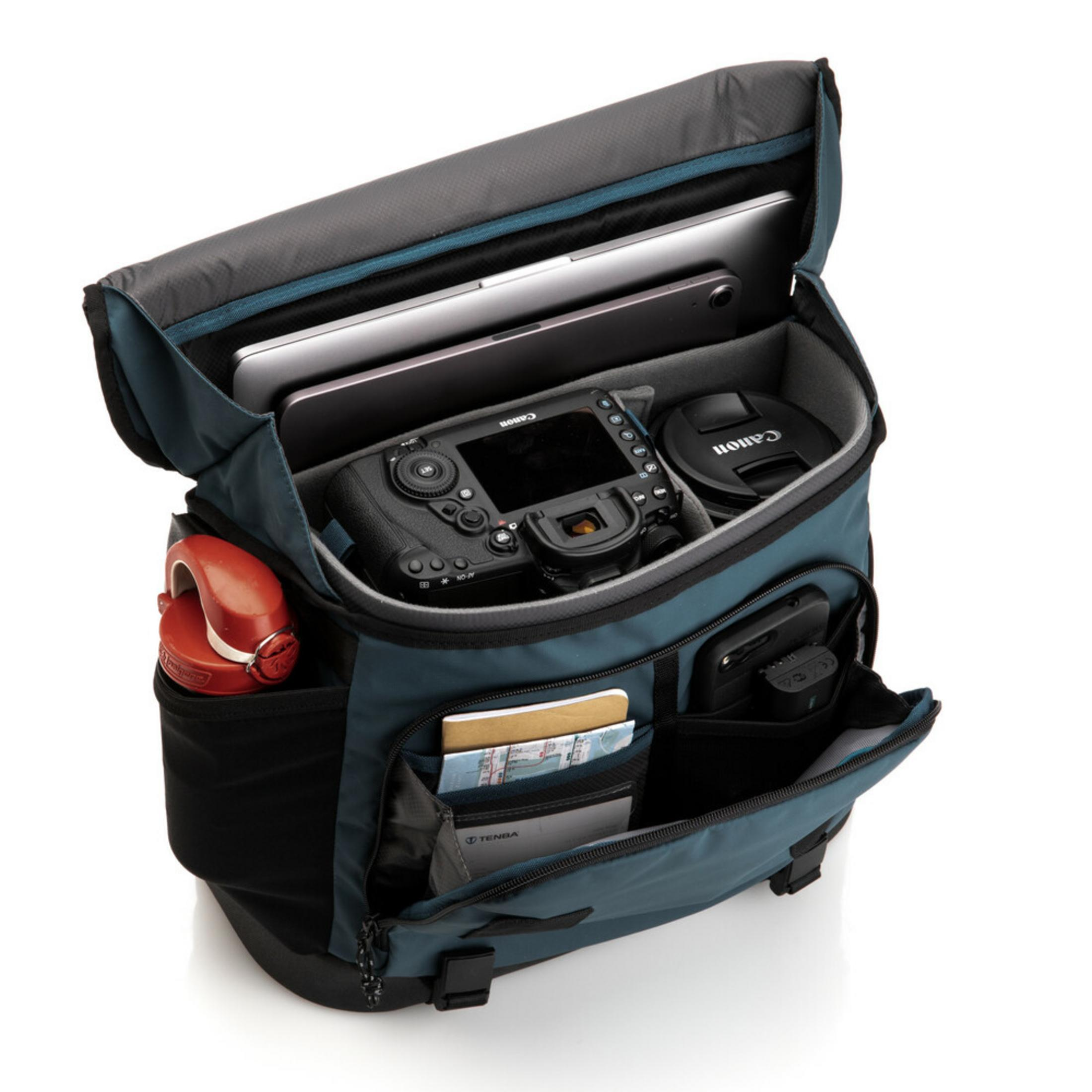A teal camera bag with a laptop, tablet, camera, lens cap, phone, and red item.