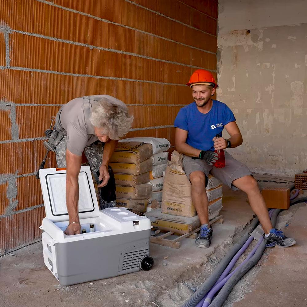 Çimento torbaları ve soğutucu ile şantiyede iki inşaat işçisi.