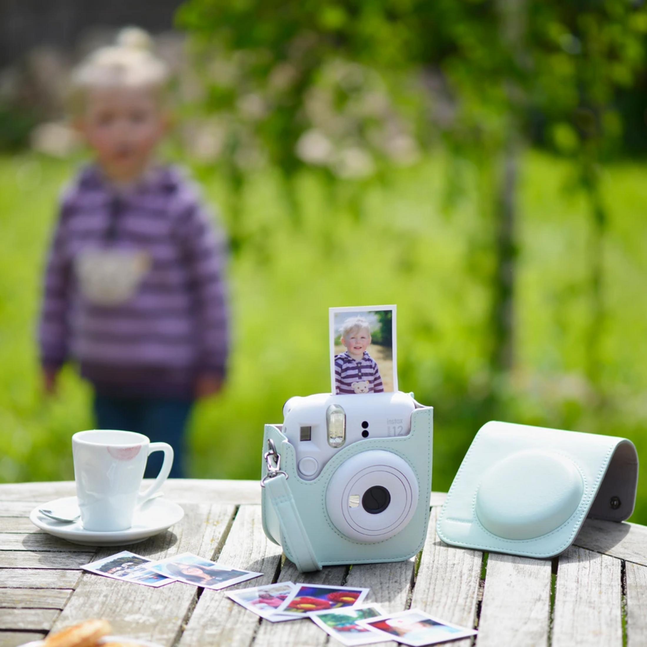 Une caméra instantanée vert menthe avec photo d'enfant est sur table bois.