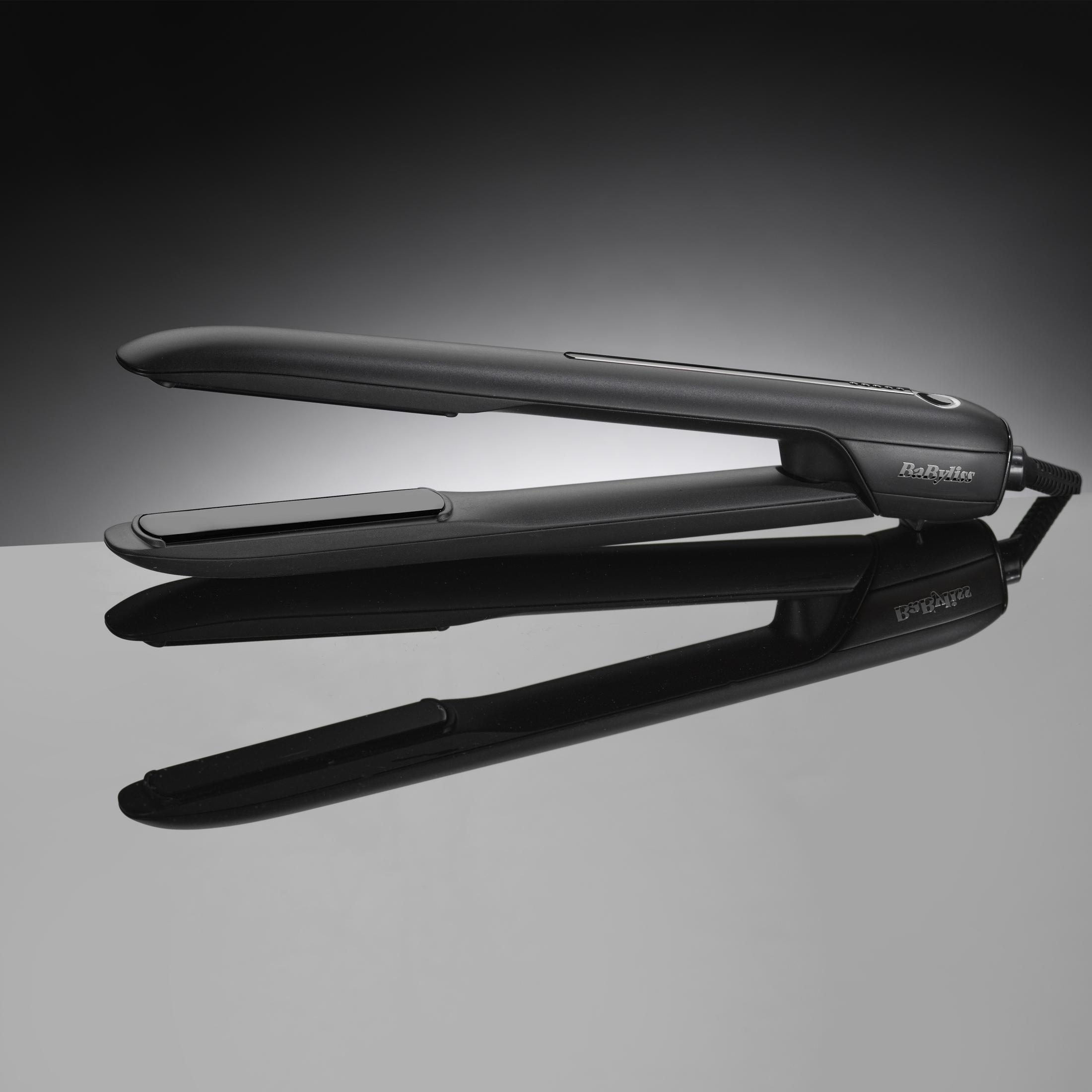 Una plancha de pelo negra descansa sobre una superficie reflectante, con luz suave desde atrás.
