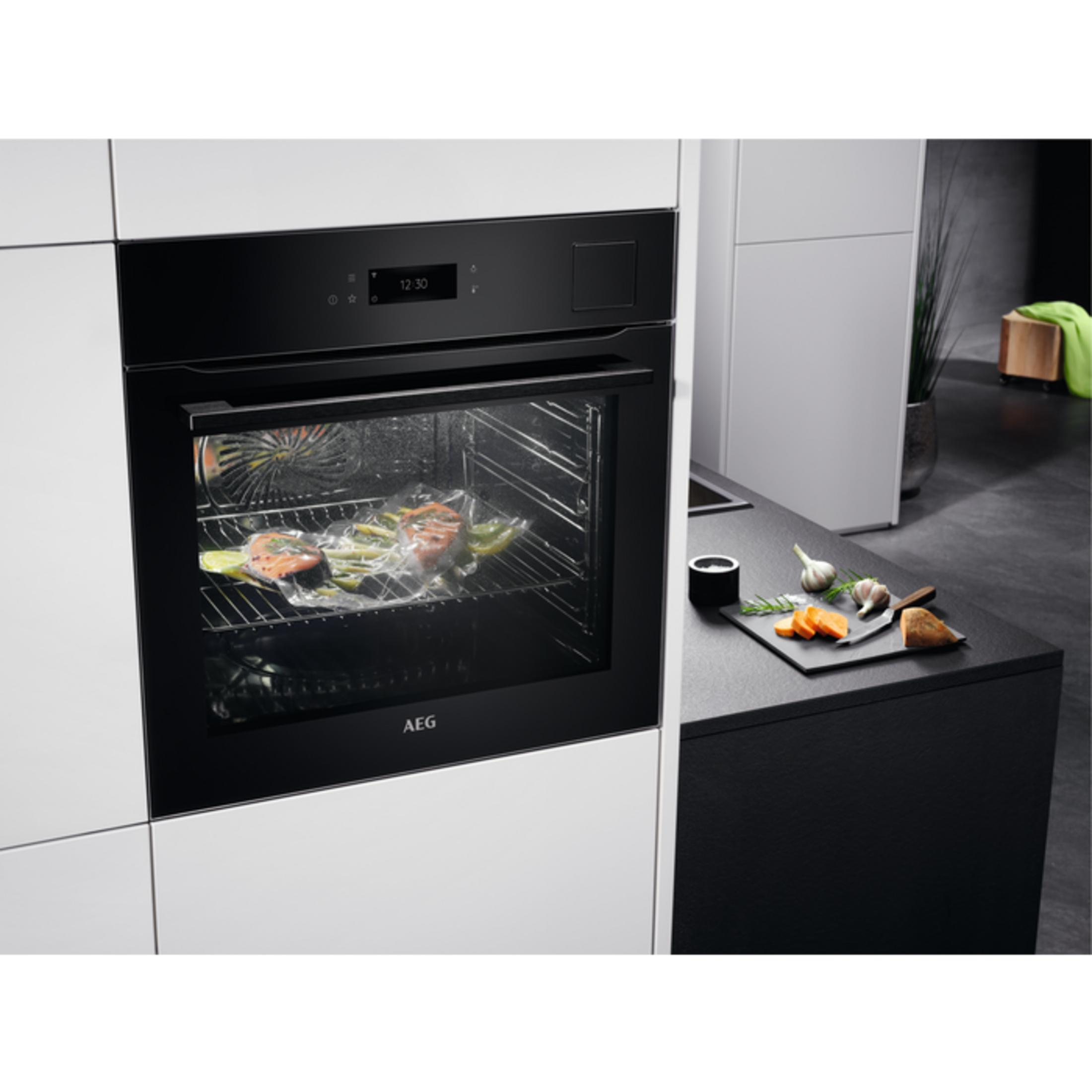A modern AEG oven with vacuum-sealed salmon and vegetables inside. Ingredients are beside it.