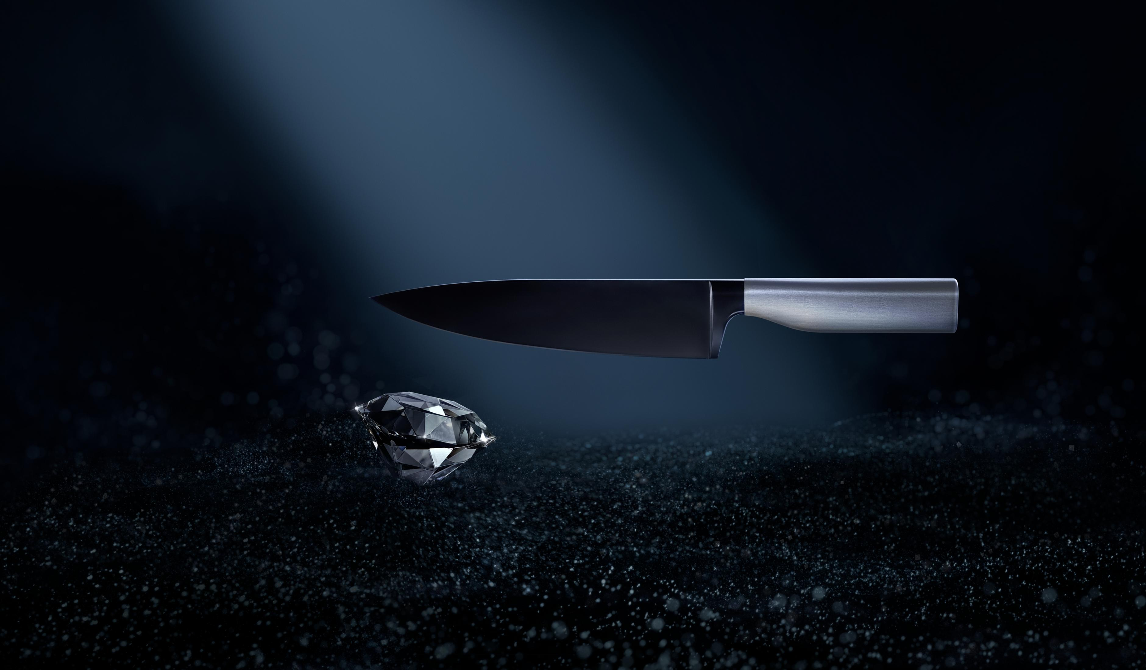 Ein dunkler Diamant und ein Küchenmesser auf dunklem, körnigem Untergrund.
