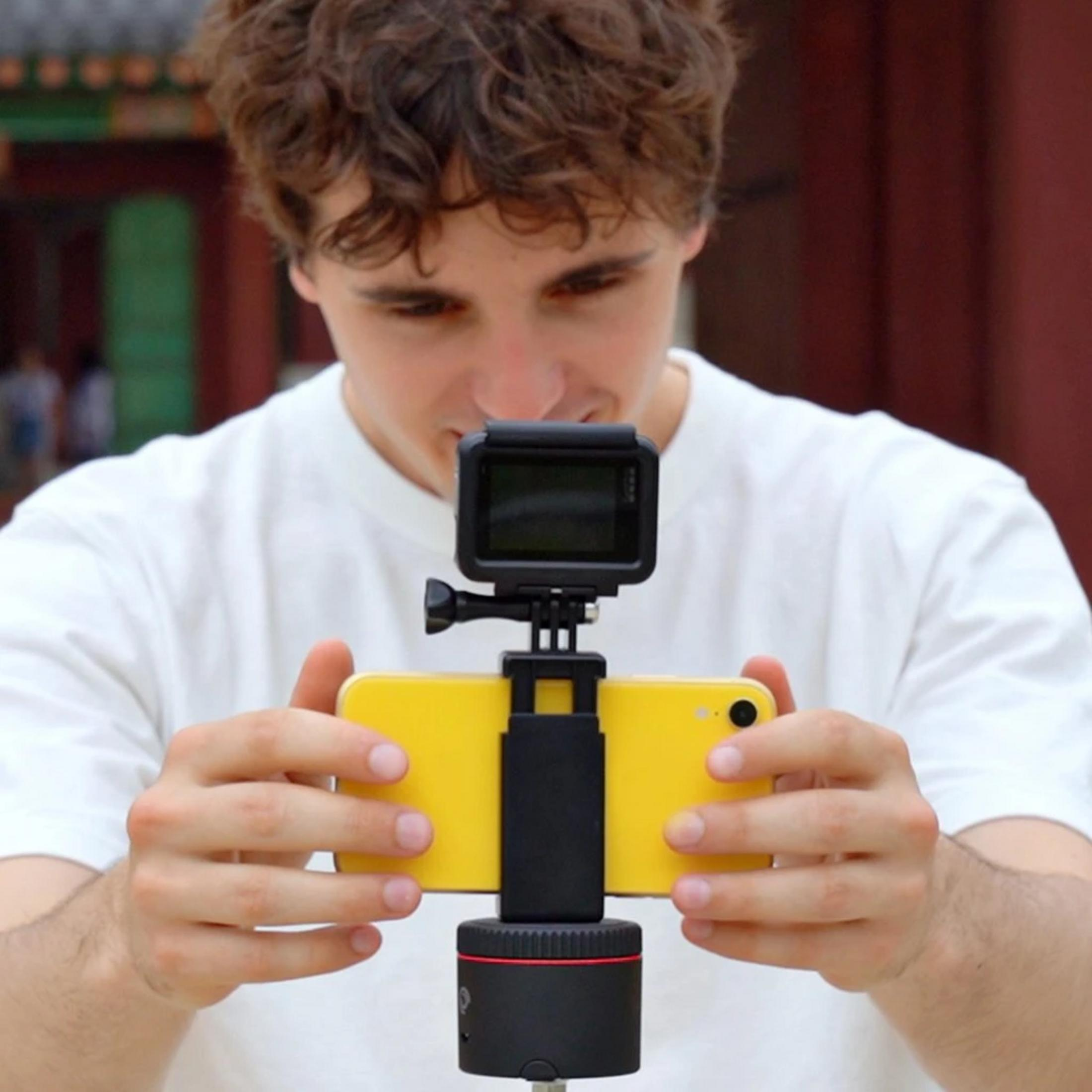 Ein Mann mit lockigem Haar hält ein gelbes Smartphone mit einer Action-Kamera.