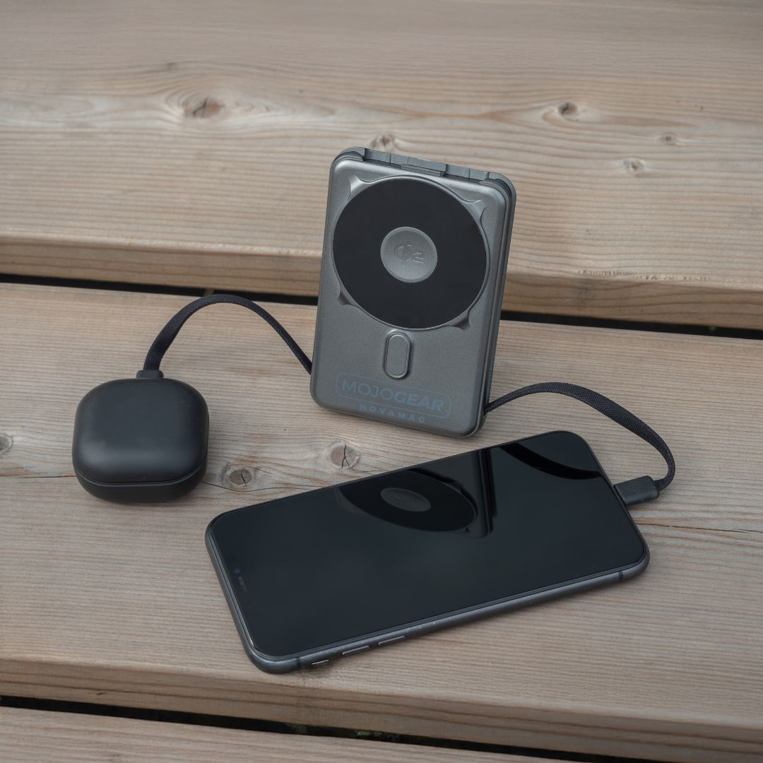Eine graue Powerbank und ein schwarzes Ladegerät, verbunden mit einem schwarzen Handy auf Holz.