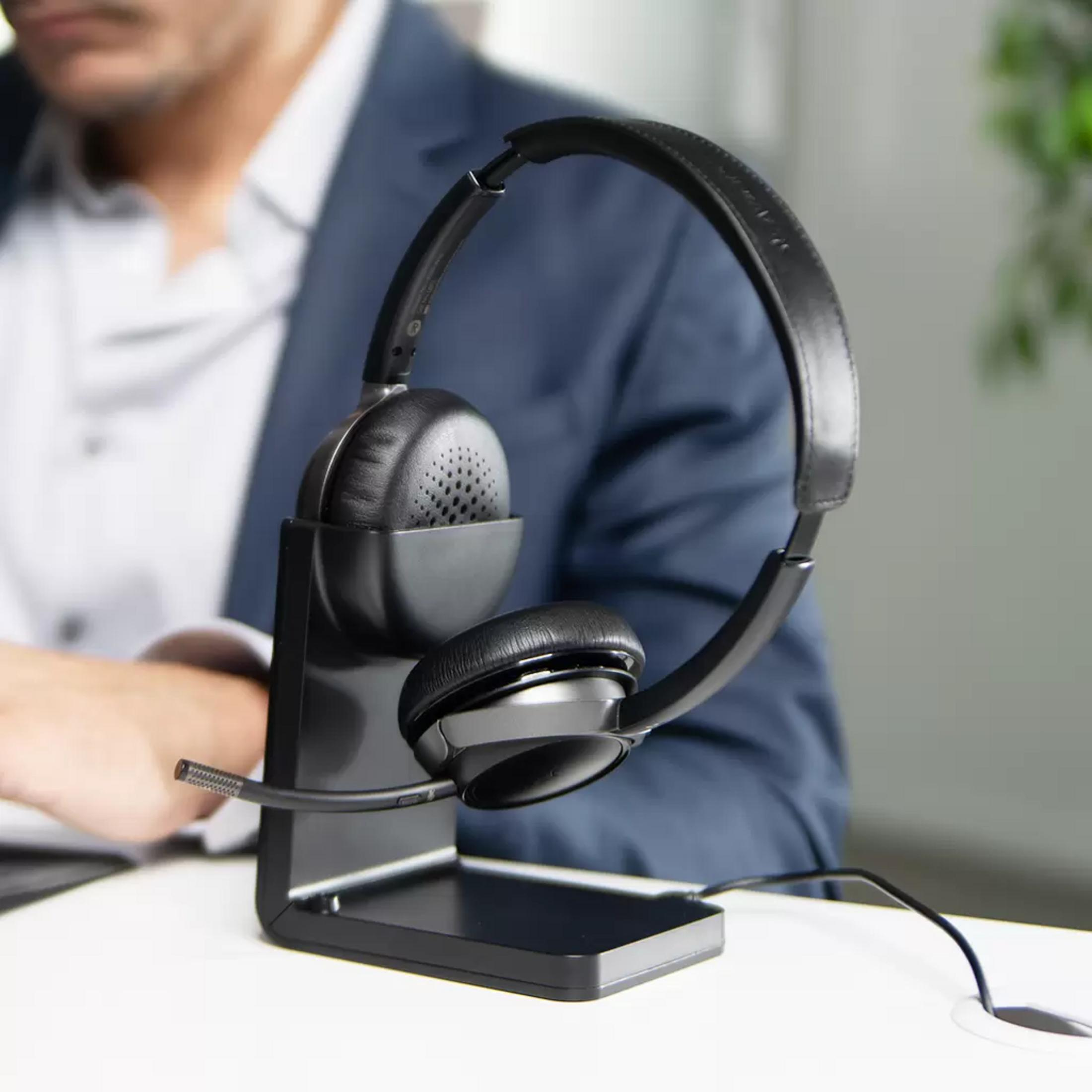 Un casque noir avec micro est sur un support. Un homme en costume est derrière.