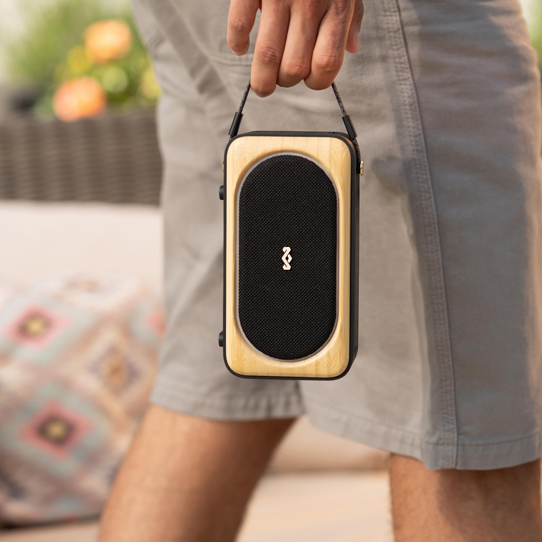Una persona tiene un altoparlante portatile con cornice in legno e griglia nera.