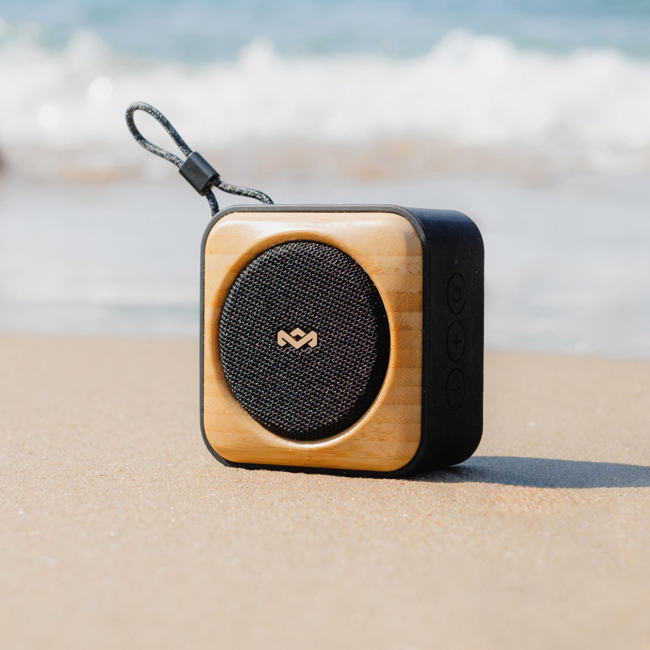 Ein tragbarer Lautsprecher mit Holzrahmen steht am Strand mit dem Meer im Hintergrund.