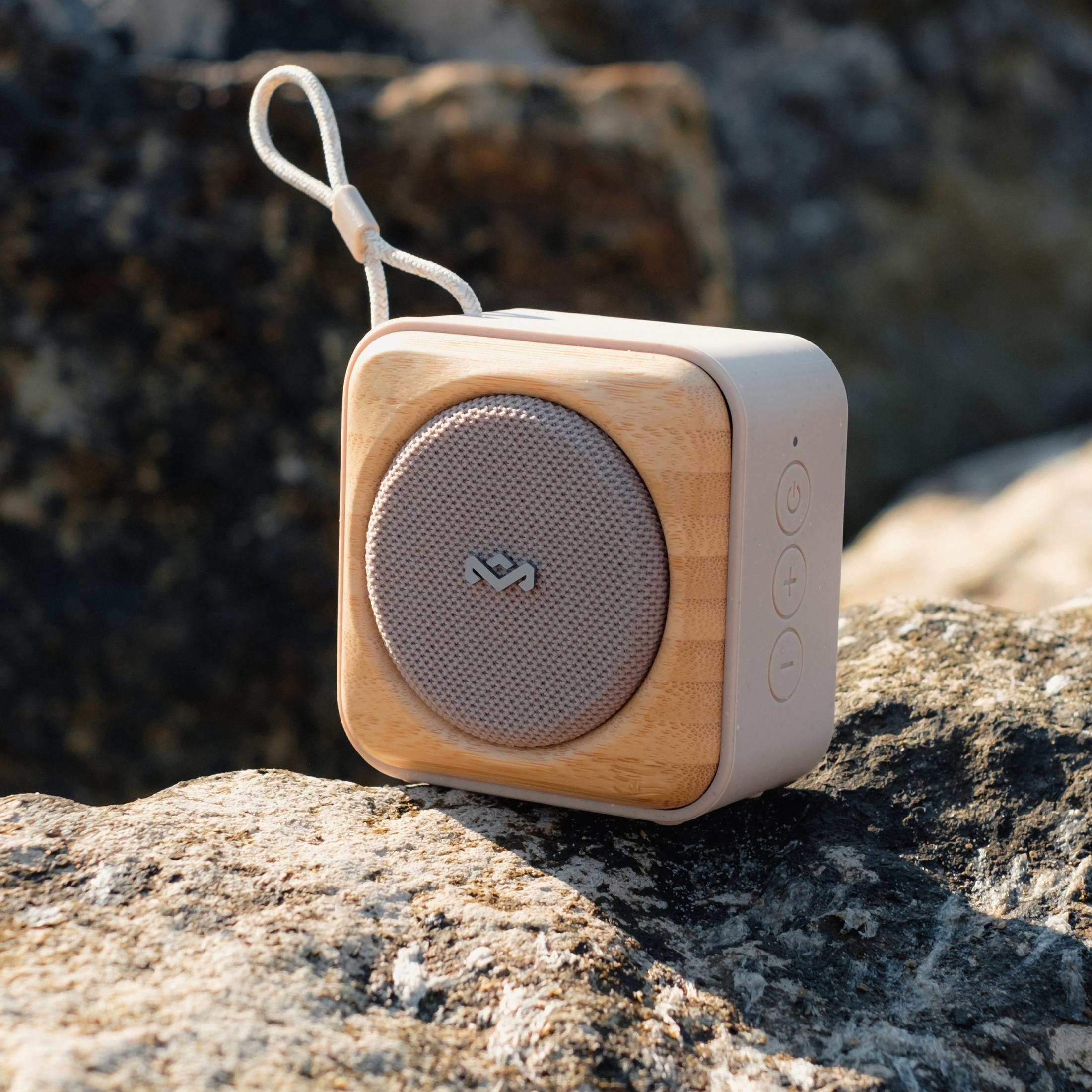 Ein kompakter Bluetooth-Lautsprecher mit Holzrahmen und Stoffgitter auf Felsen.
