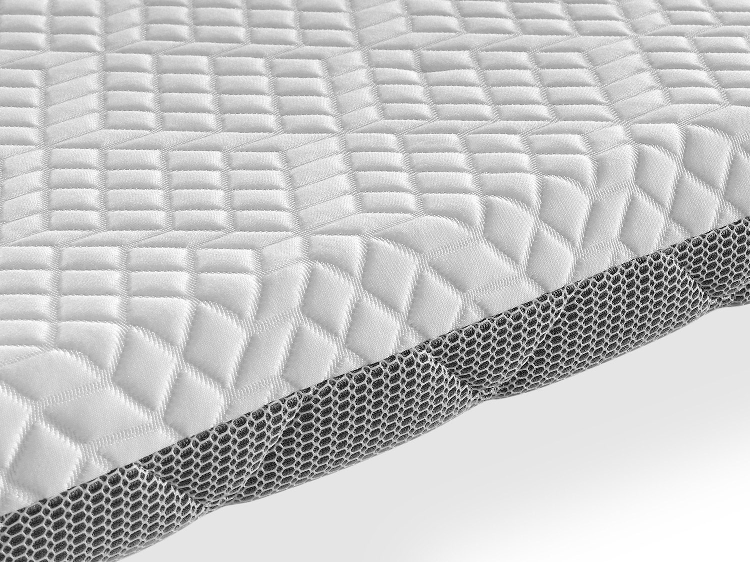 Primer plano de una superficie de colchón blanca acolchada con un lateral de patrón de panal gris.