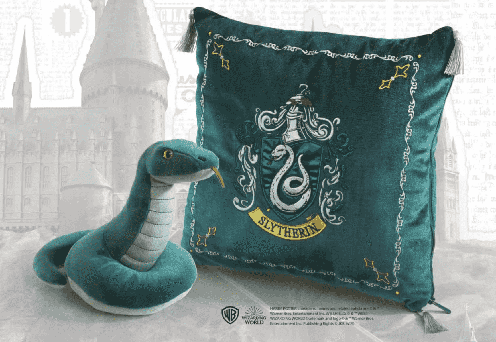 Un peluche de serpiente verde y un cojín con el escudo de Slytherin sobre fondo de castillo.