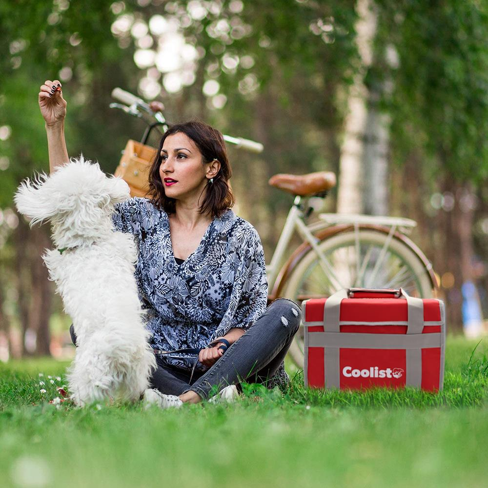 Kadın parkta beyaz köpekle oynuyor, bisiklet ve çanta var.