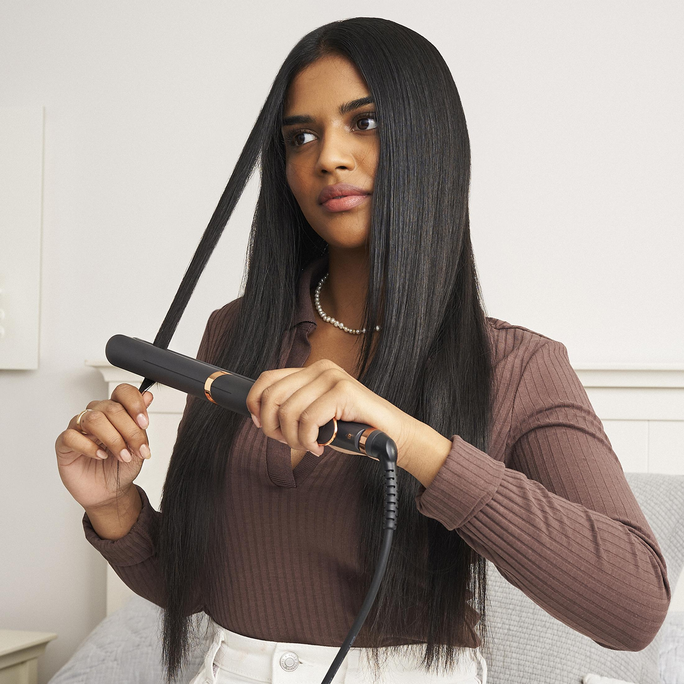 Una donna con lunghi capelli scuri si piastra i capelli con una piastra nera e oro rosa.