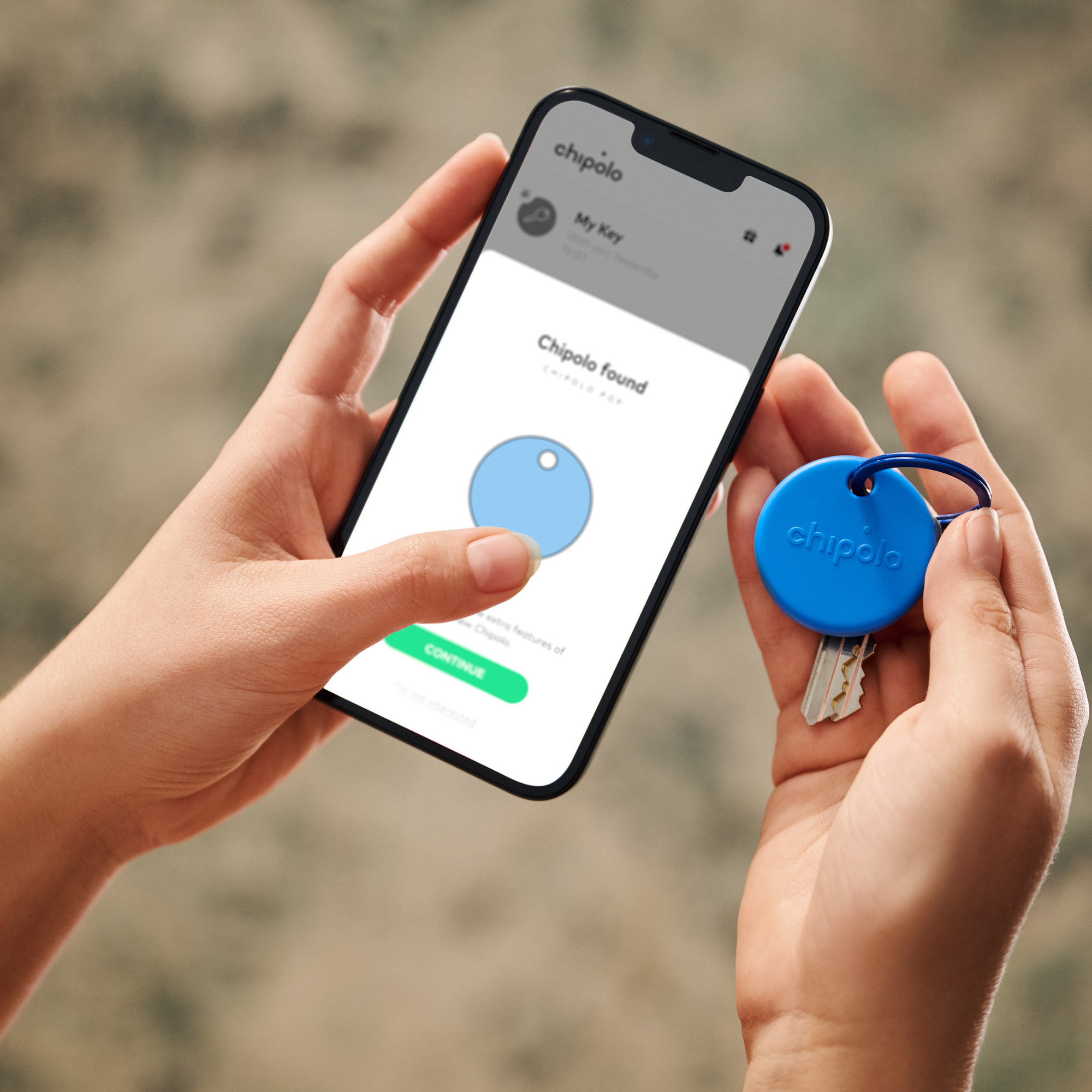 Hands holding smartphone with Chipolo app, blue Chipolo tag with key.